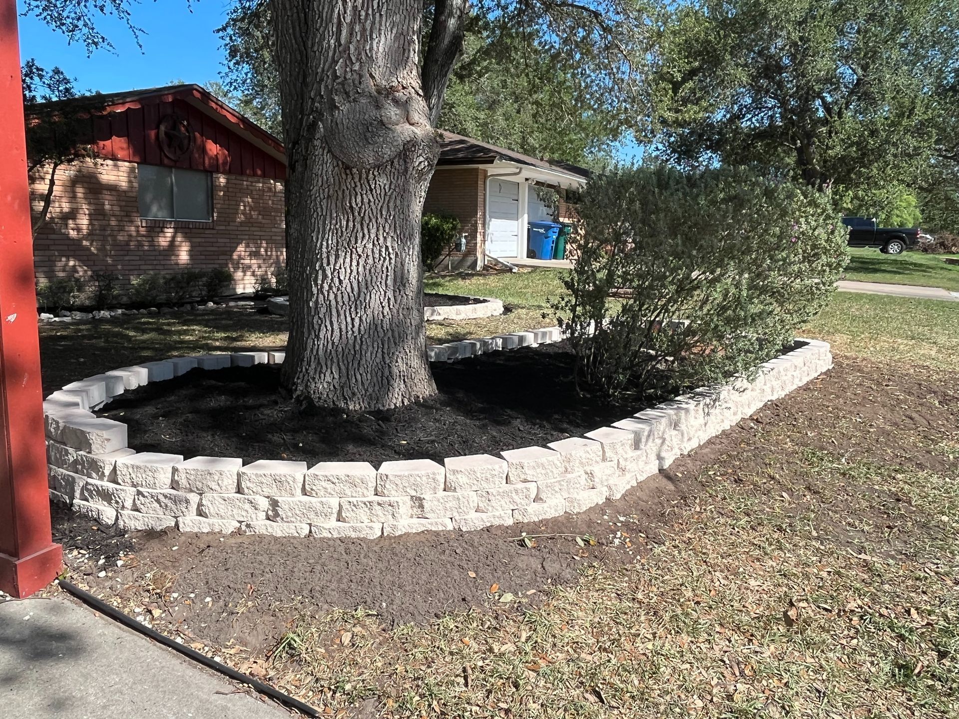 A tree is surrounded by a stone wall in front of a house.