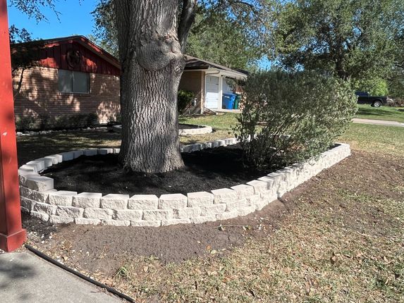 A tree is surrounded by a stone wall in front of a house.