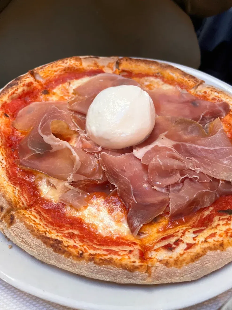 Pizza con prosciutto e una palla di burrata bianca su un piatto