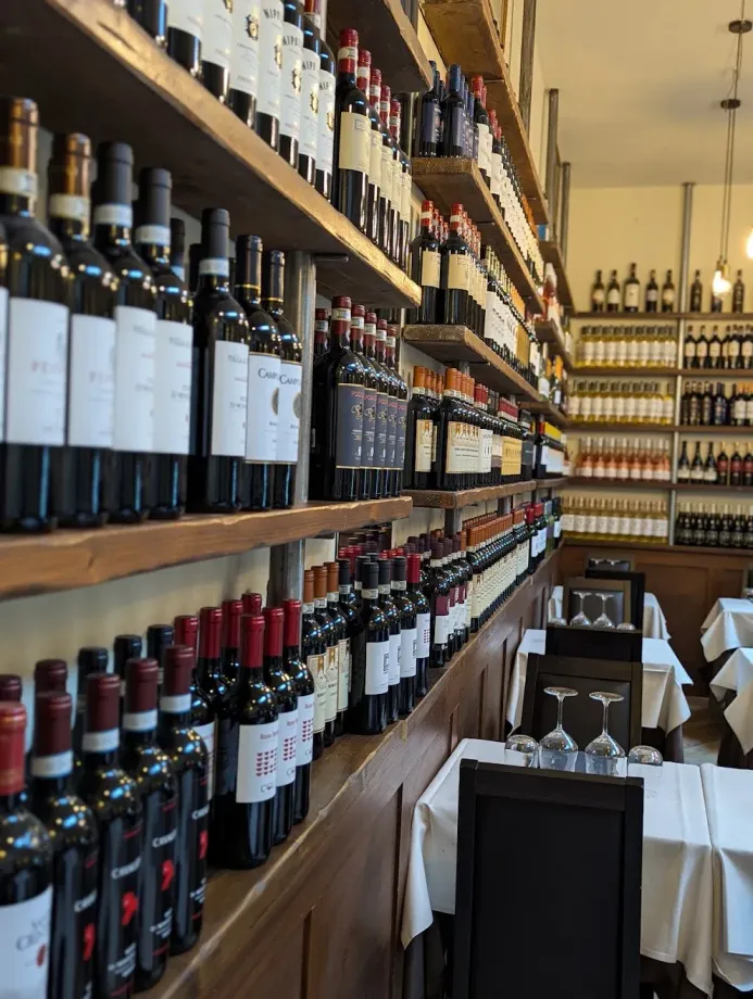 Bottiglie di vino allineate su scaffali di legno in un'accogliente sala da pranzo di un ristorante, con tavoli e sedie apparecchiati.