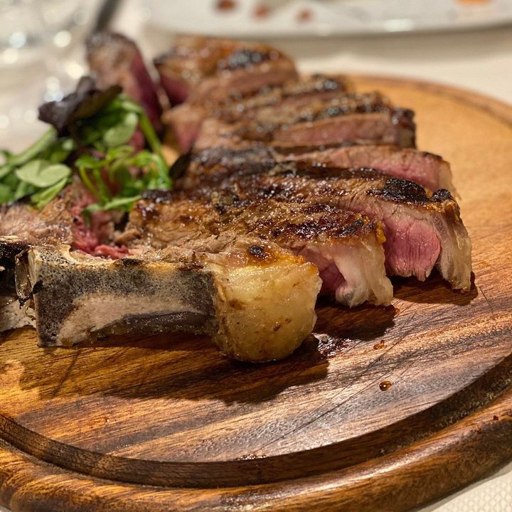 Fettine di bistecca grigliata su un tagliere di legno con crosta bruciacchiata e verdure di contorno.