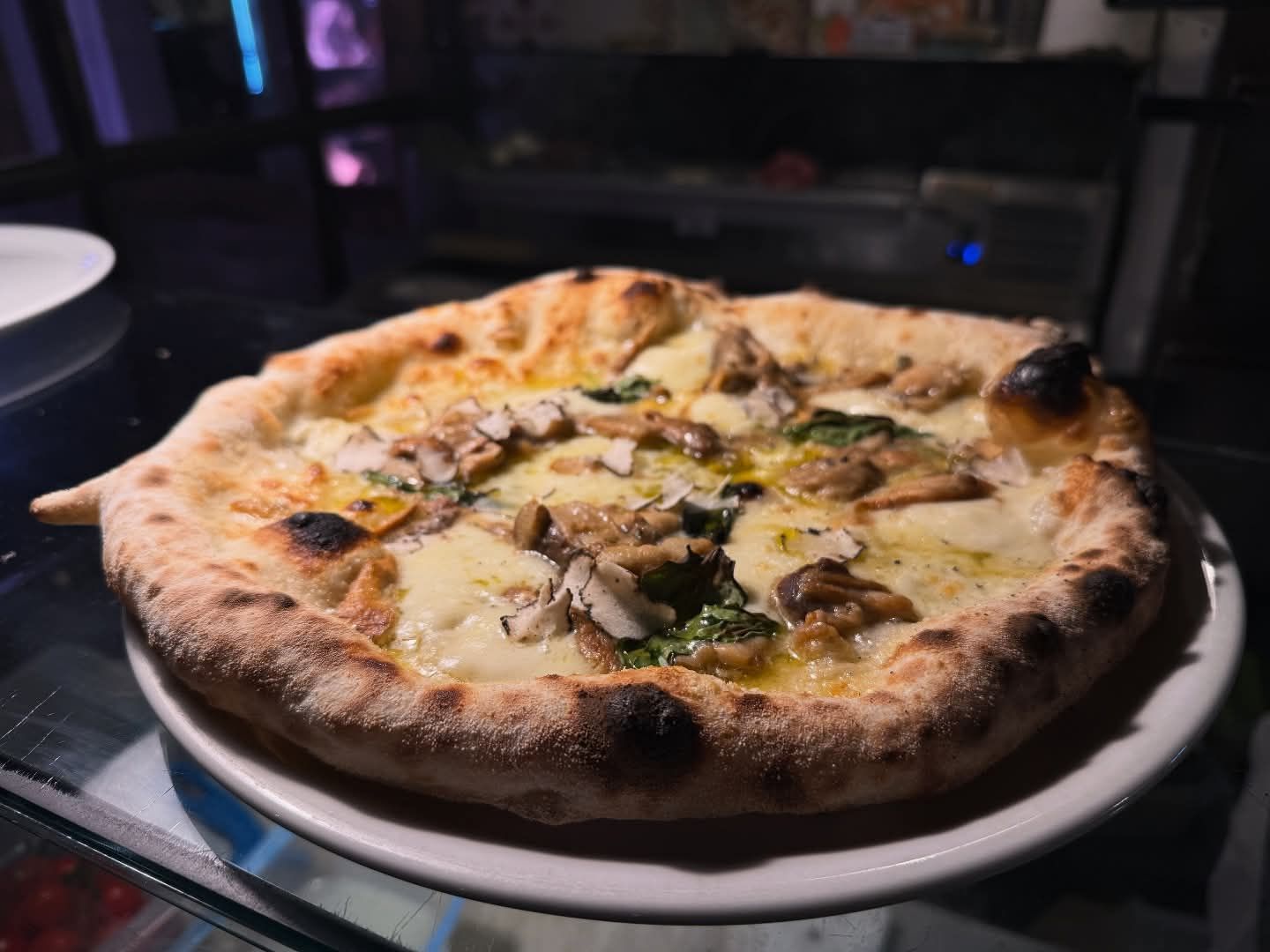 Pizza su un piatto bianco, con formaggio fuso e funghi, su un tavolo in una stanza poco illuminata