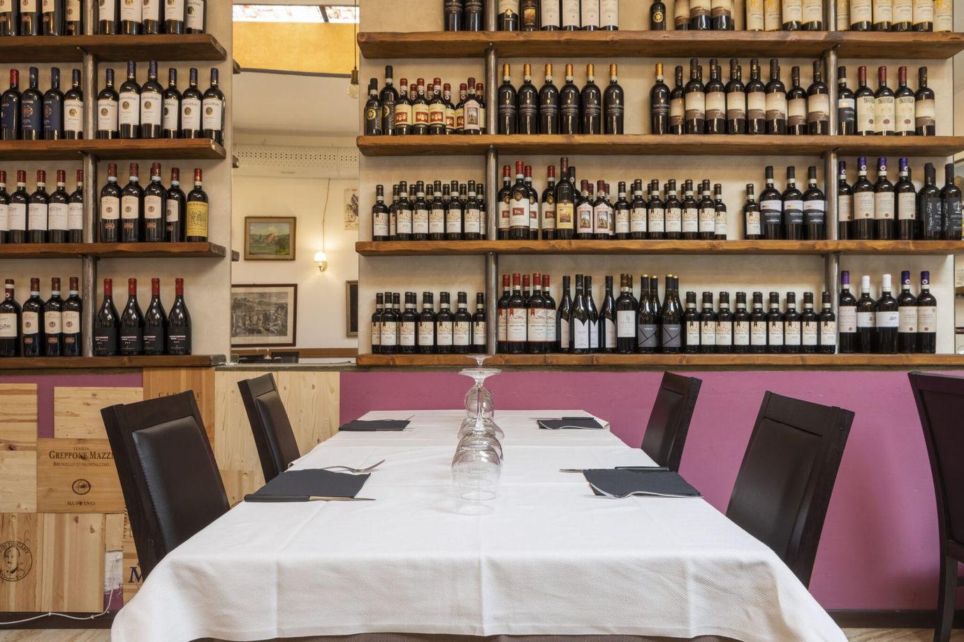 Sala da pranzo del ristorante con tavoli apparecchiati con tovaglie bianche e bottiglie di vino esposte su scaffali dietro il bancone.