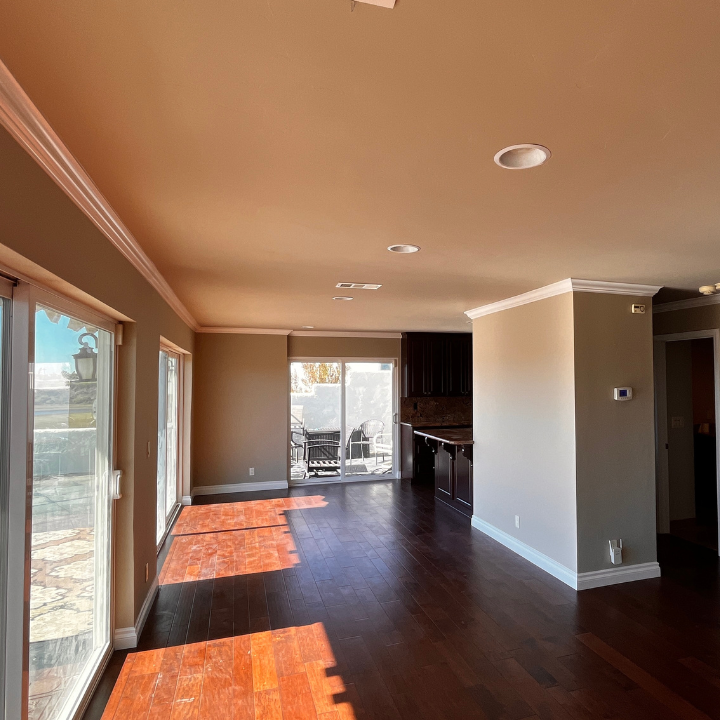 Spacious living room with dark wood floors, sliding glass doors, and brown walls.