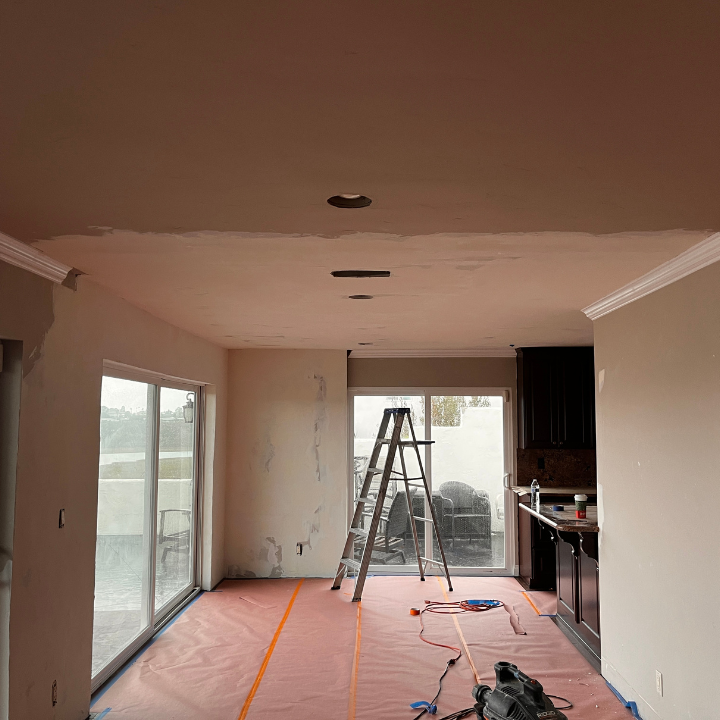 Interior room under renovation, with ladder, drop cloth, and exposed ceiling details.