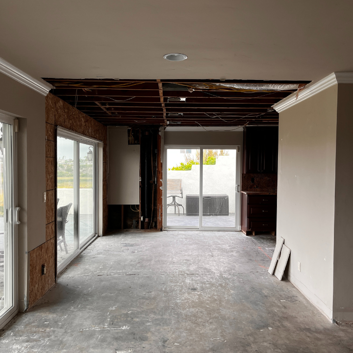 Interior view of a room under construction with exposed ceiling beams and a concrete floor; sliding glass doors.