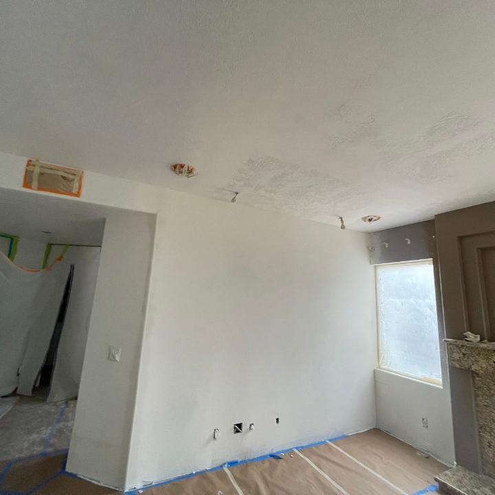 Interior room with white walls, exposed outlets, masked window, and paper-covered floor, prepared for painting.