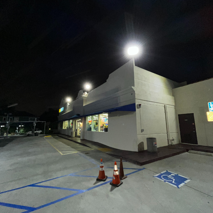 Night shot of a brightly lit convenience store with blue trim, cones, and a handicap parking space.