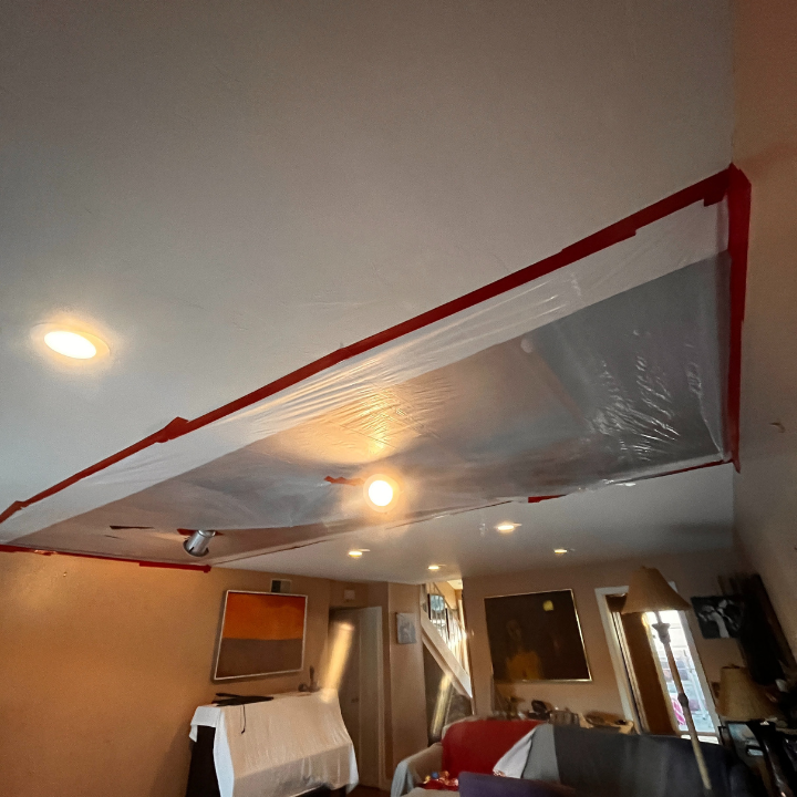 Ceiling with plastic sheeting taped to it, covering an area. Red tape used for sealing.