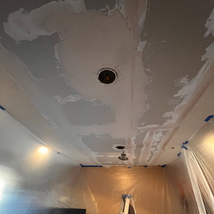 Ceiling drywall repair: Spackling around light fixtures, room covered in plastic sheeting.