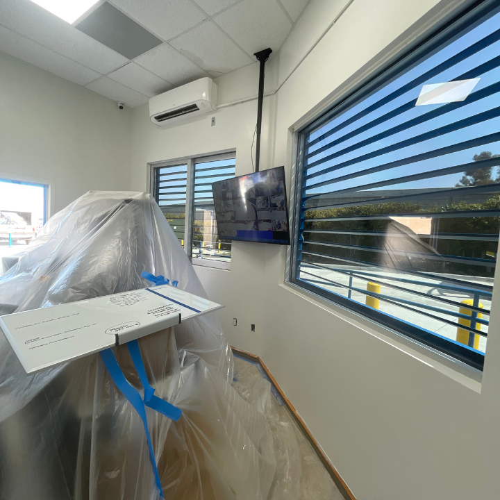 Interior room with covered equipment, mounted TV, window with blinds, and air conditioning unit.
