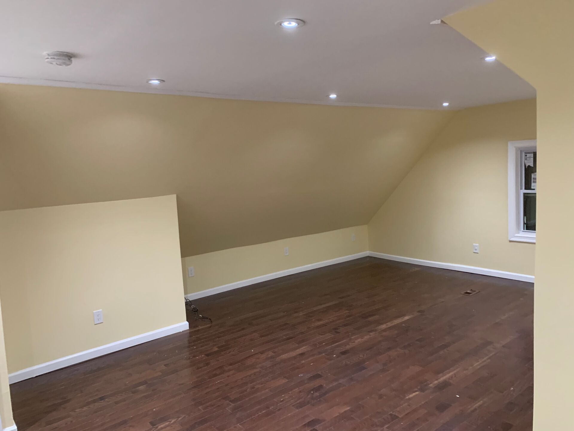 Empty room with hardwood floors, sloped walls, and recessed lighting.