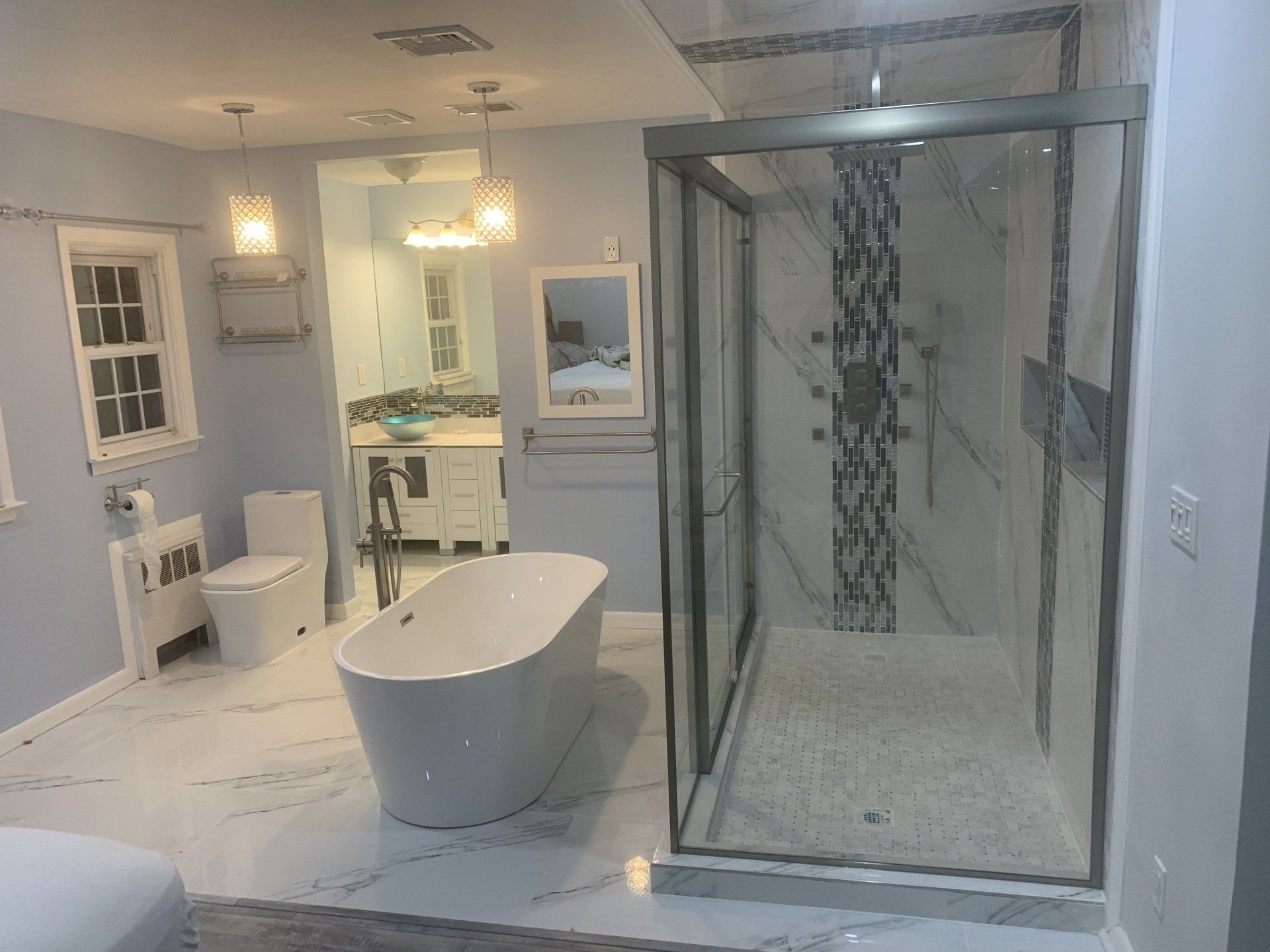 Spacious modern bathroom with a white soaking tub, large glass shower, and marble floors. Light blue walls.