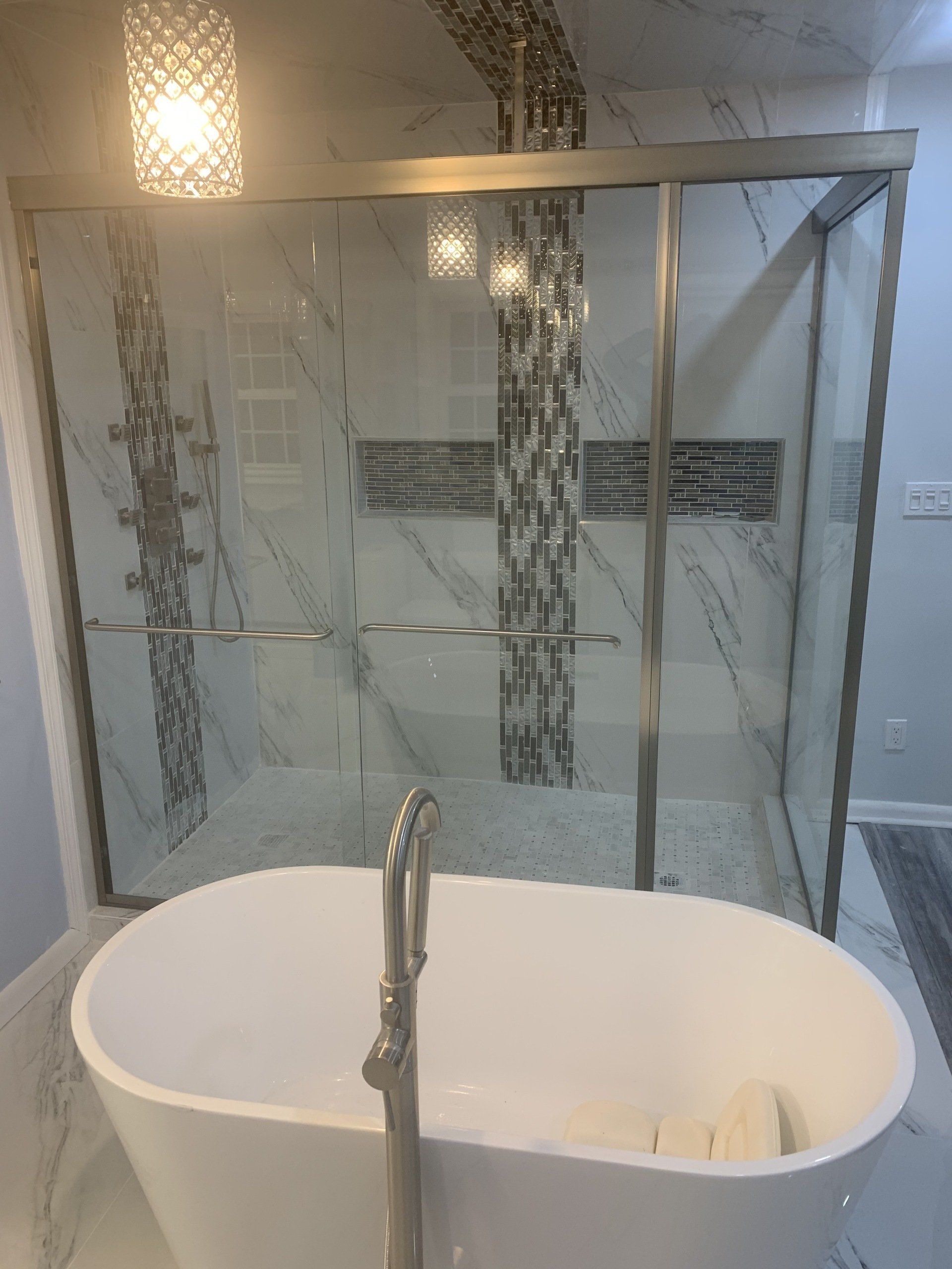 Modern bathroom: white freestanding tub in front of a glass shower with decorative tile.