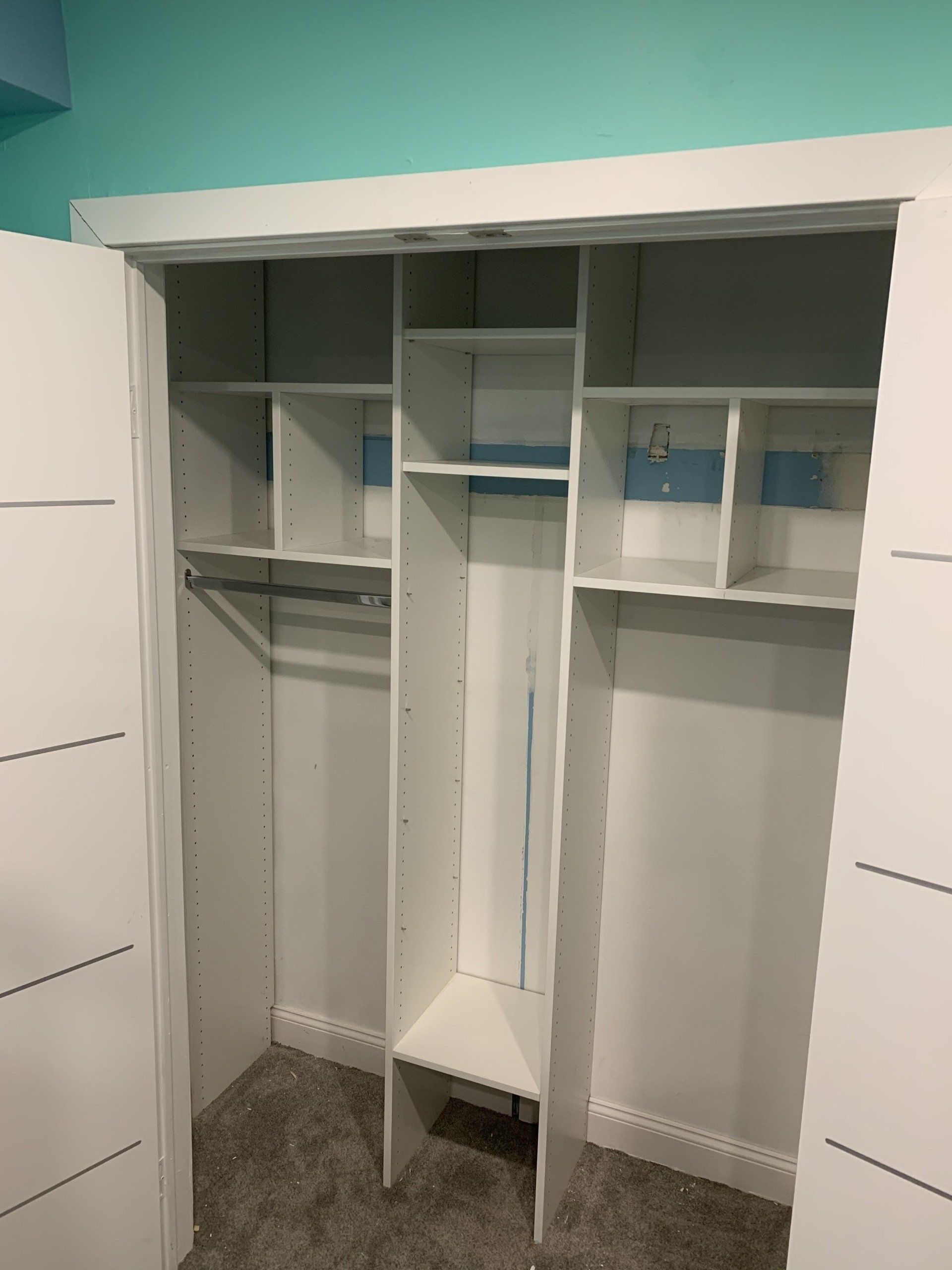 White closet with shelves, rods, and compartments, teal wall in the background.