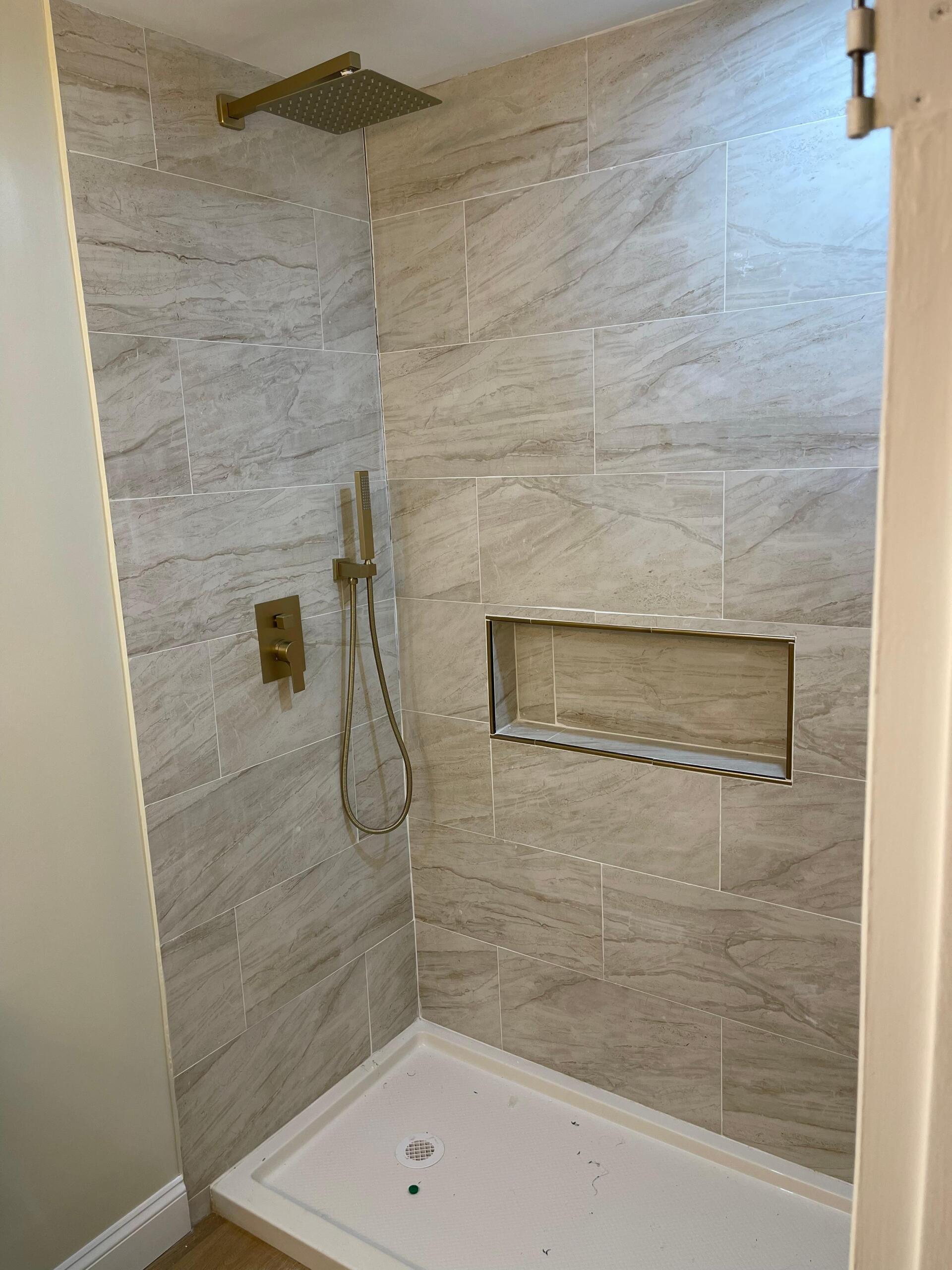 Shower with light-colored, patterned tile, gold fixtures, and a recessed shelf.
