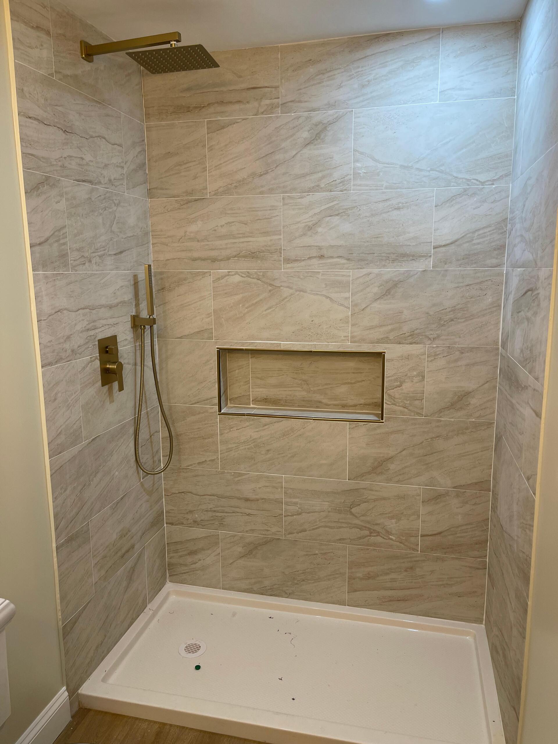 A tiled shower with gold fixtures, a built-in shelf, and a white base.