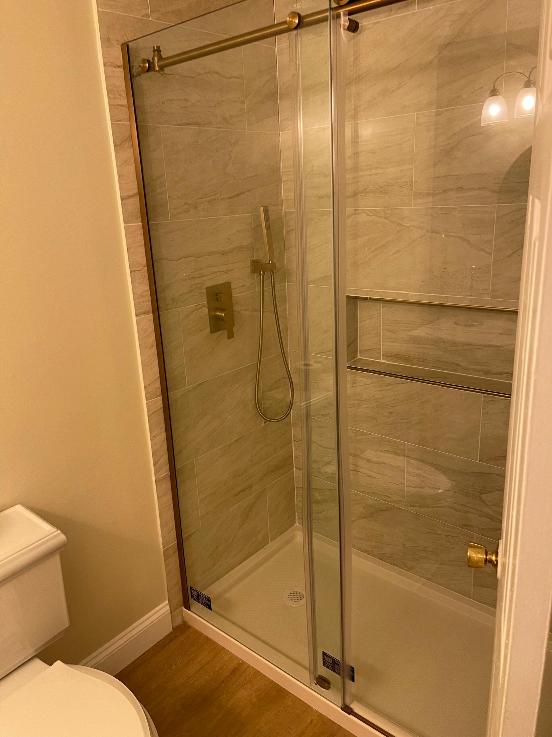 Shower with glass doors and gold fixtures, beige tile walls.