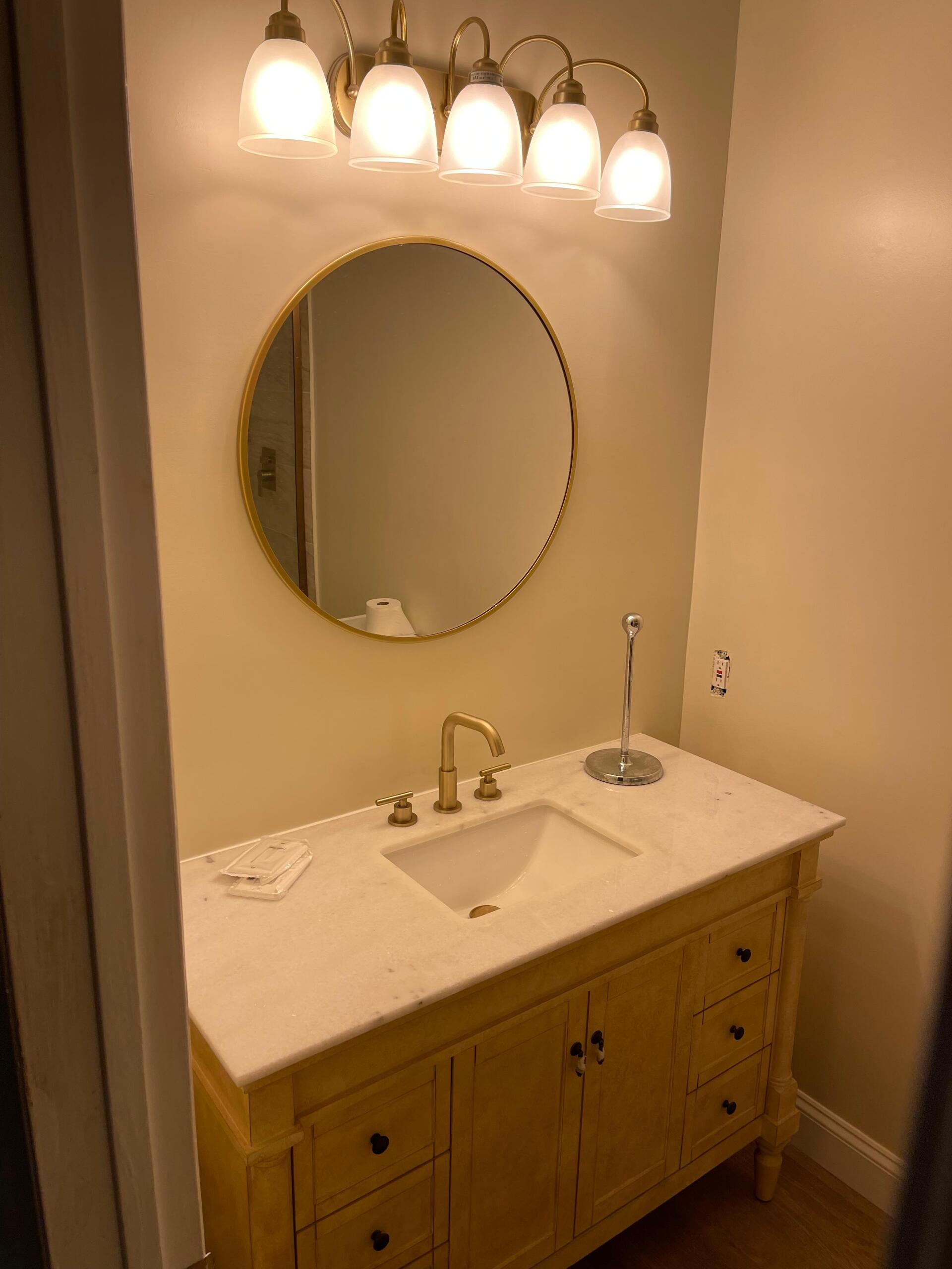 Bathroom vanity with gold-framed mirror, gold faucet and light fixture, and yellow cabinet.