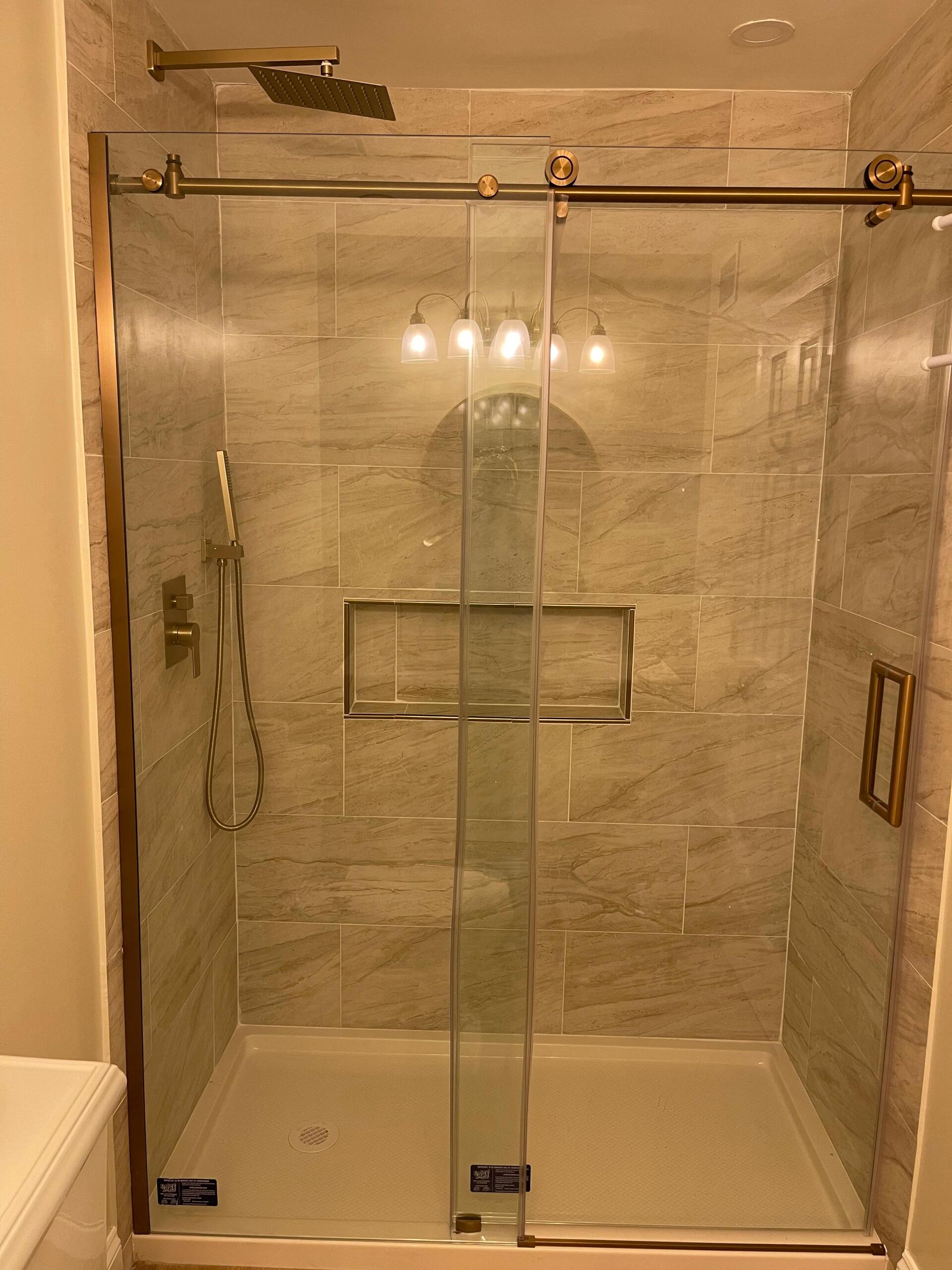 Glass shower enclosure with gold fixtures and tiled walls.