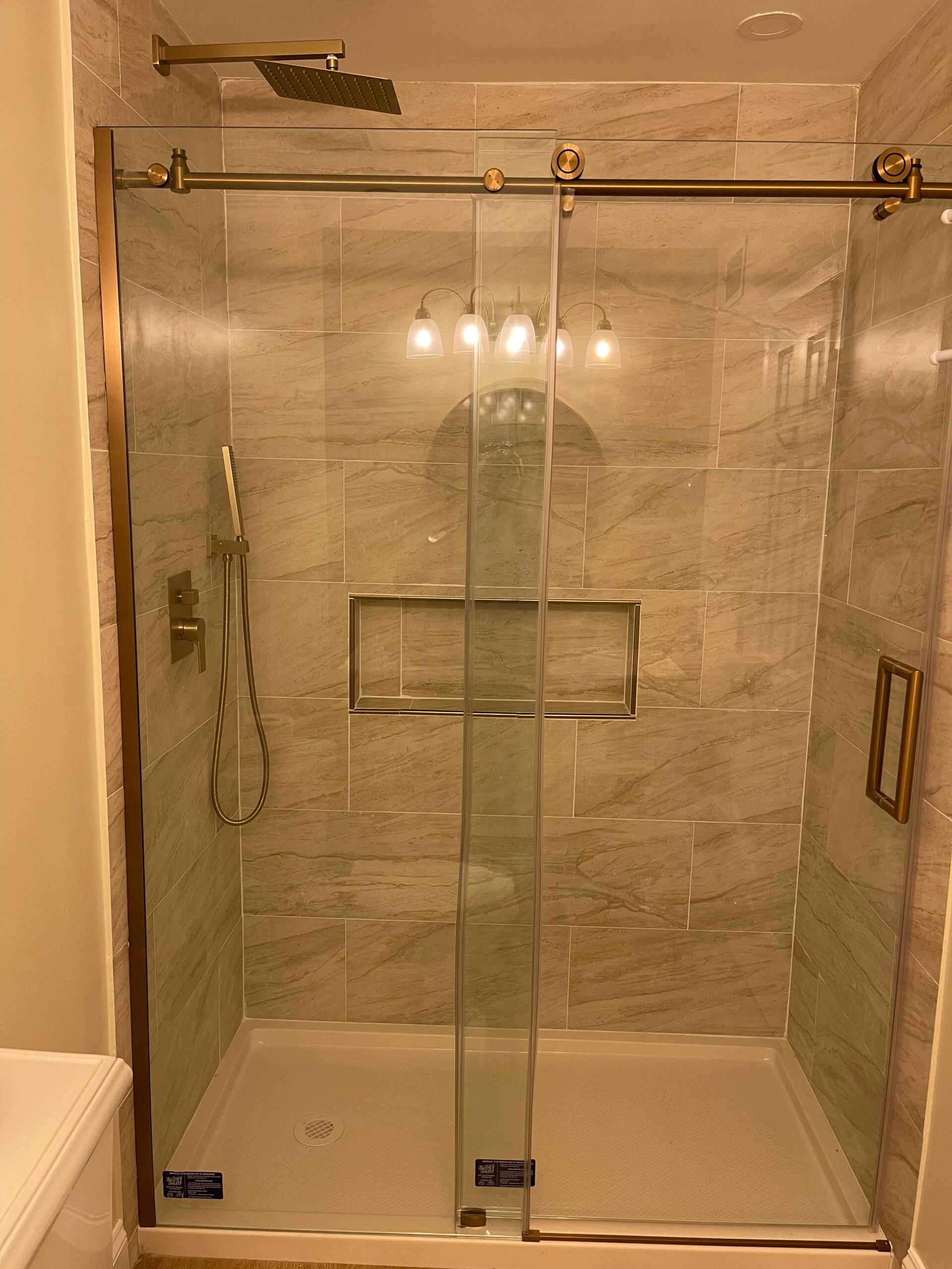 Shower stall with glass doors, bronze fixtures, and light-colored tile.