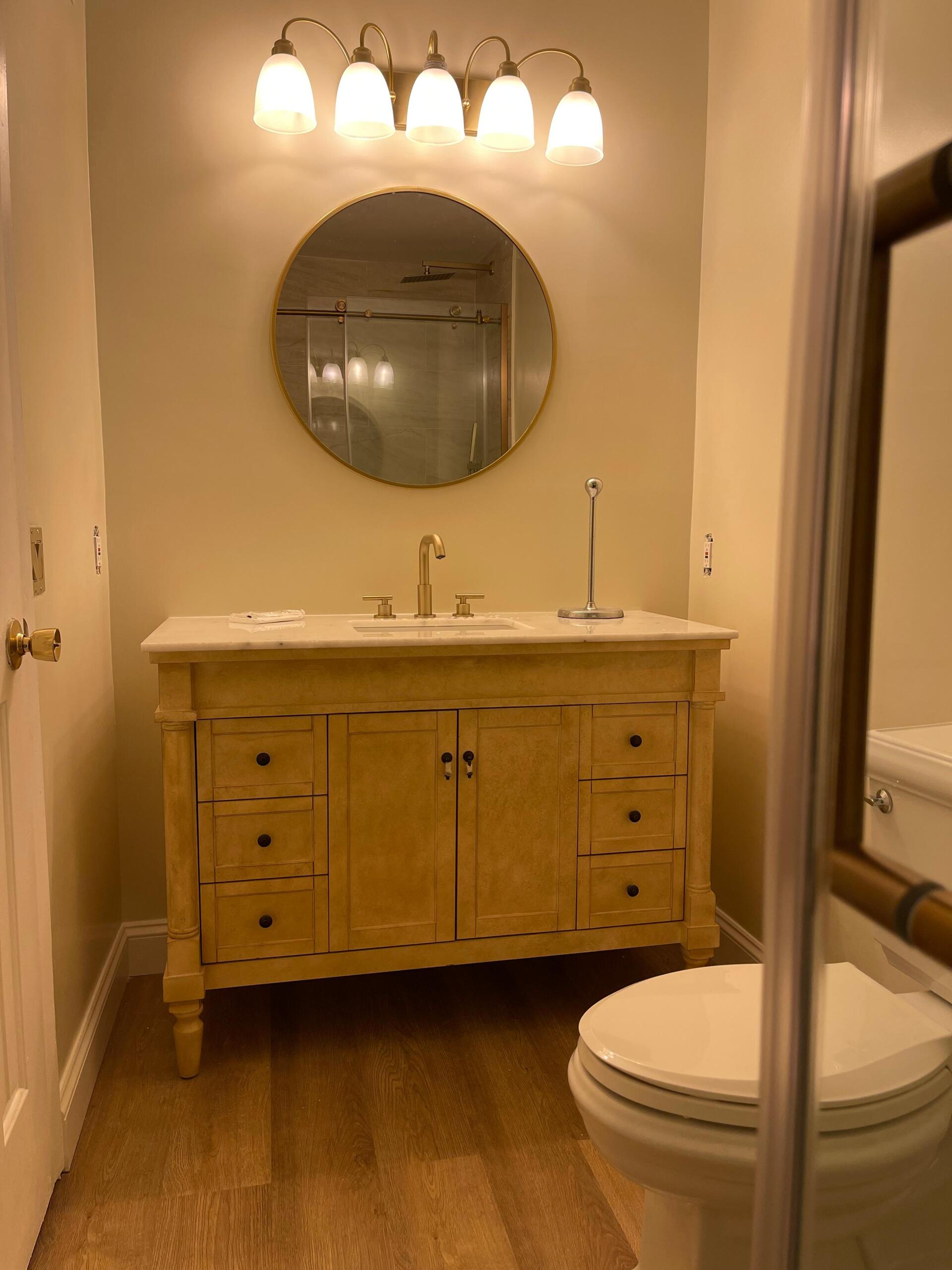 Bathroom with light-colored vanity, round mirror, and a toilet. Warm-toned walls and floor.