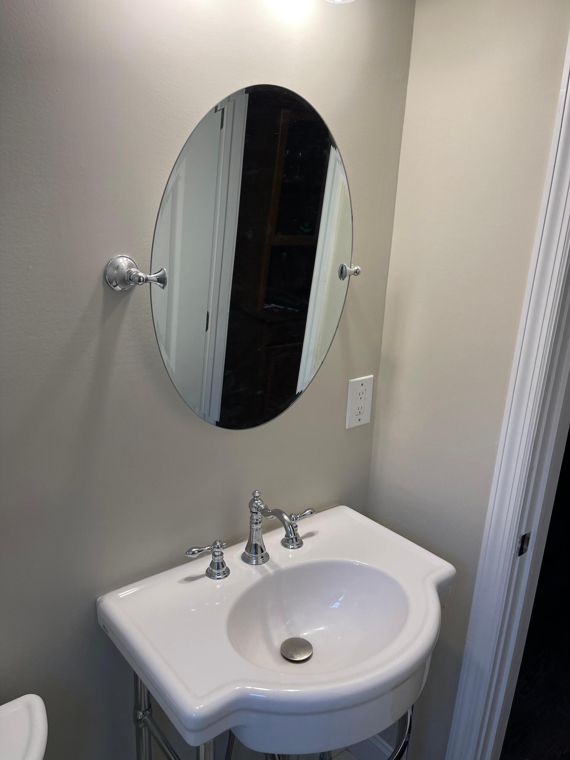 Oval mirror above a white sink in a light-colored bathroom.