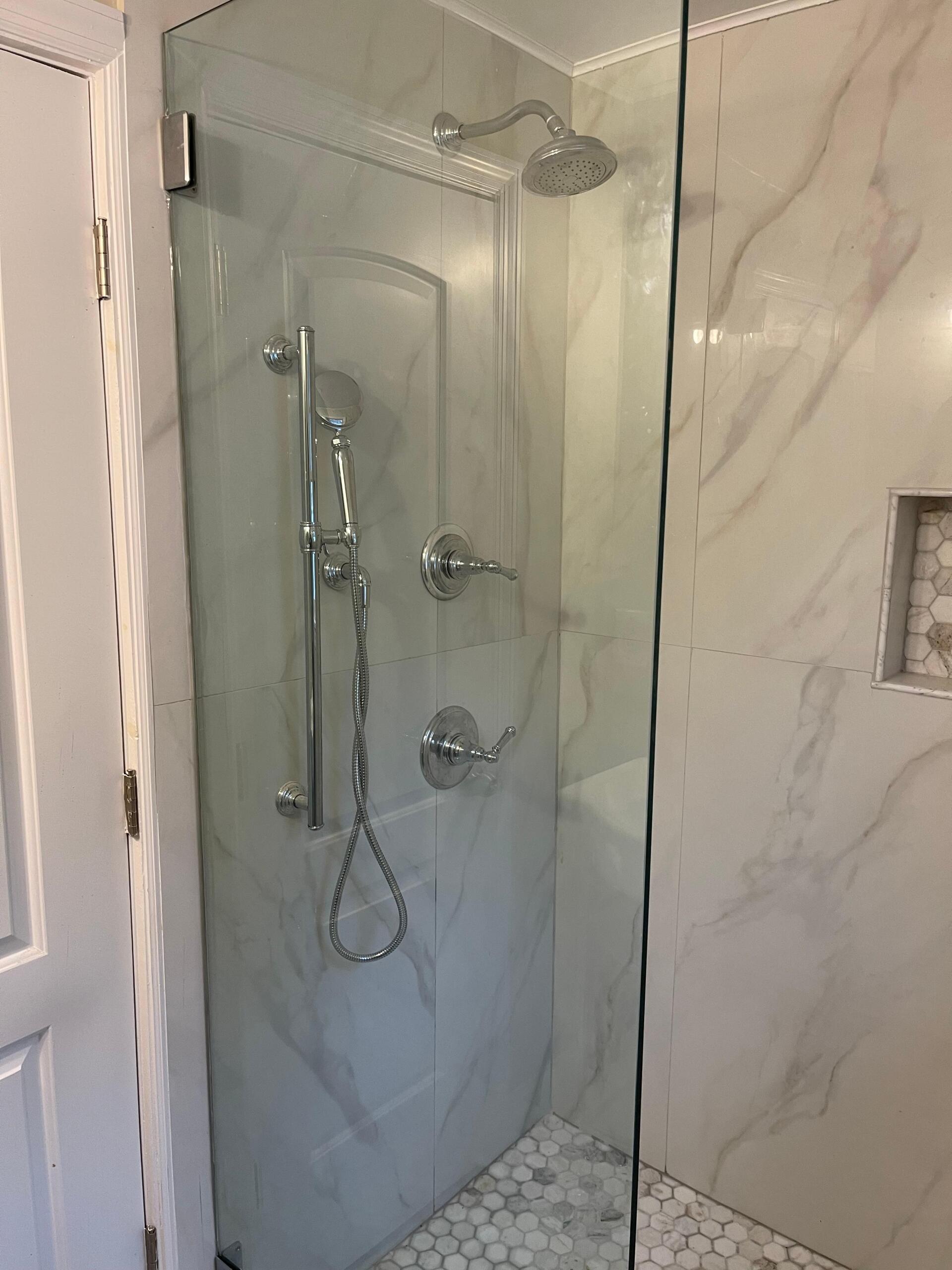 Glass shower enclosure with chrome fixtures and marble-like tile in a bathroom.
