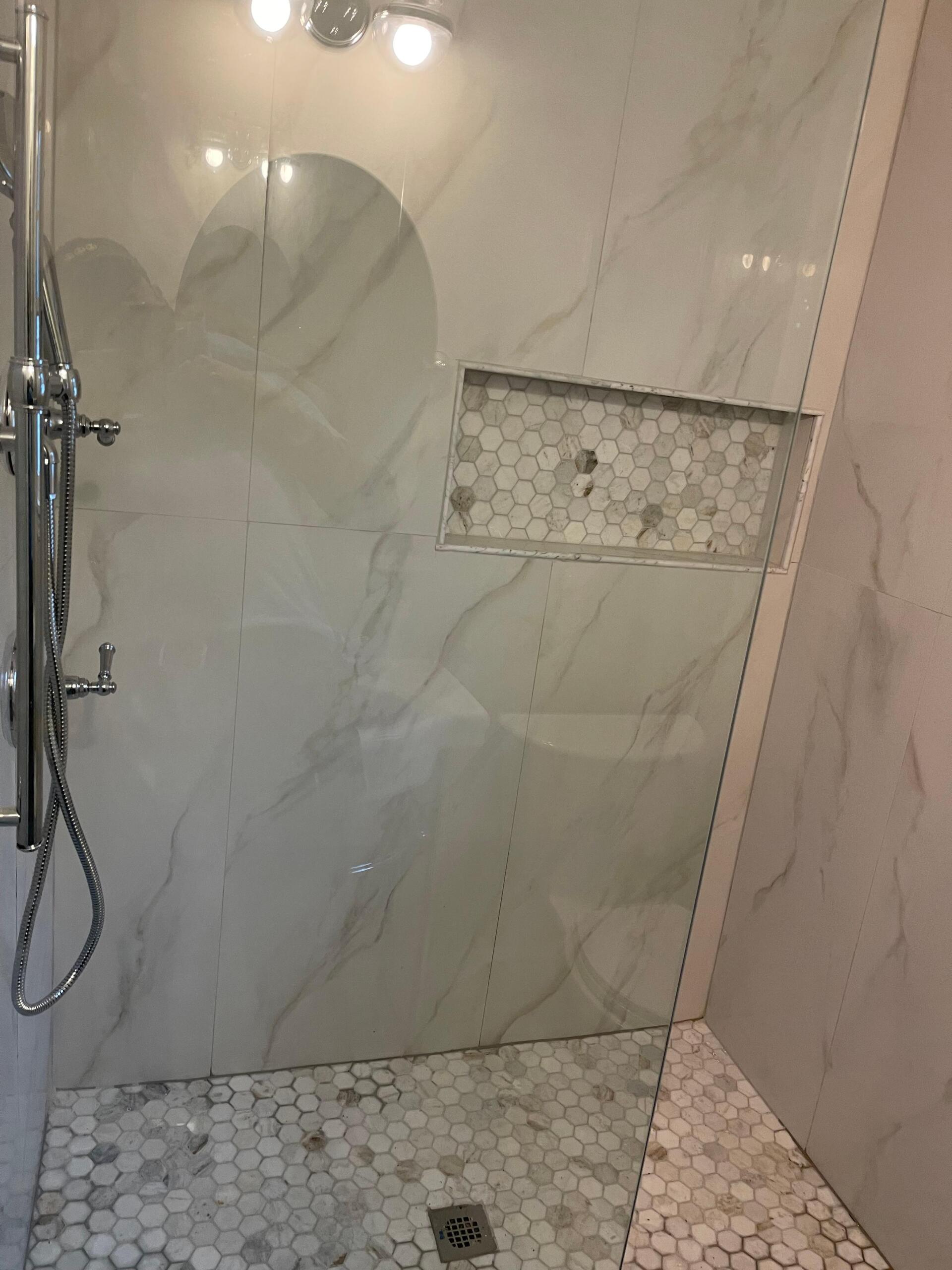 Shower with white marble tiles, including a built-in hexagonal tile niche and polished chrome fixtures.