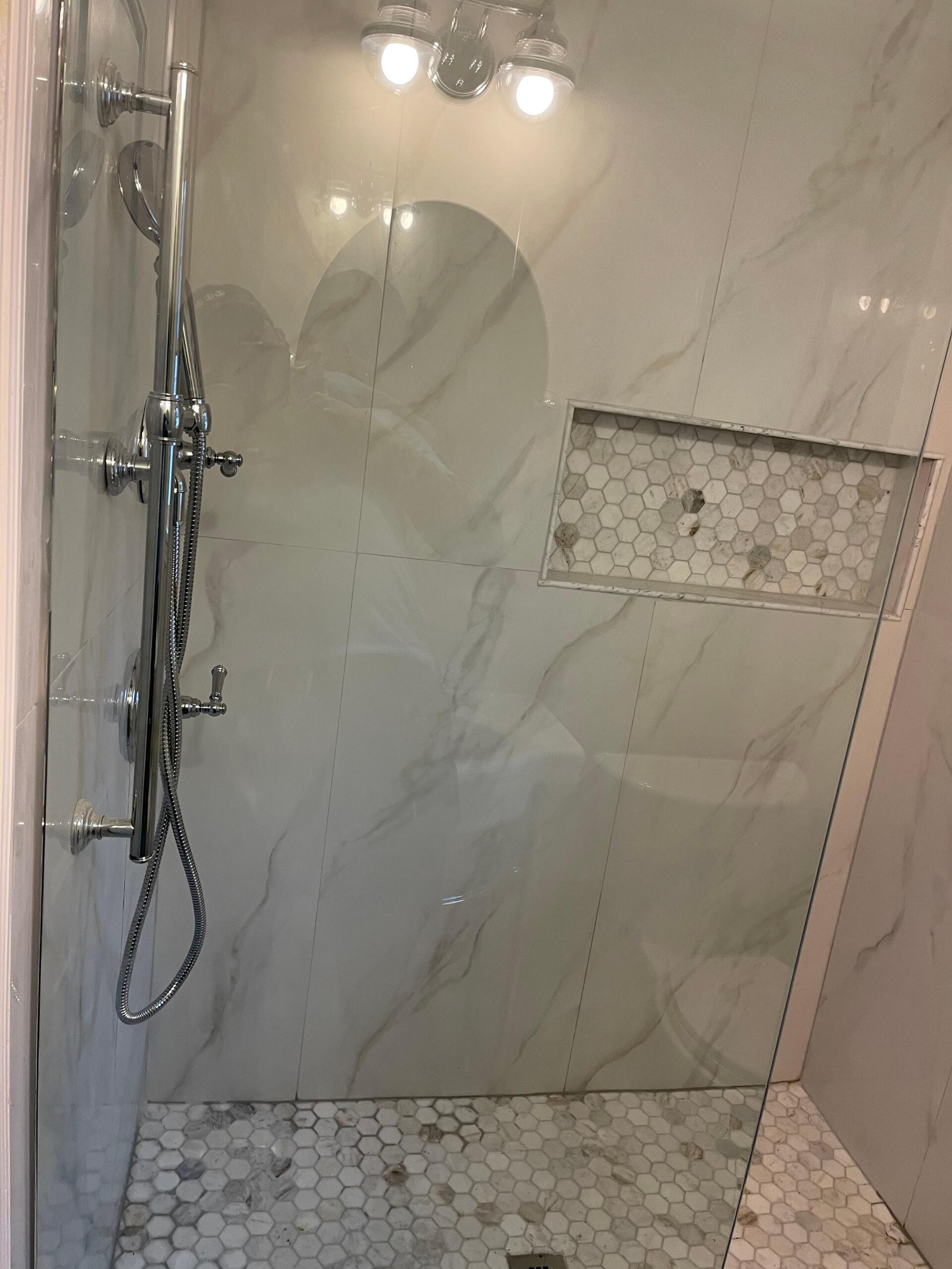 Shower with marble-look tile, glass door, and hexagon tile floor. Silver fixtures and built-in shelf.