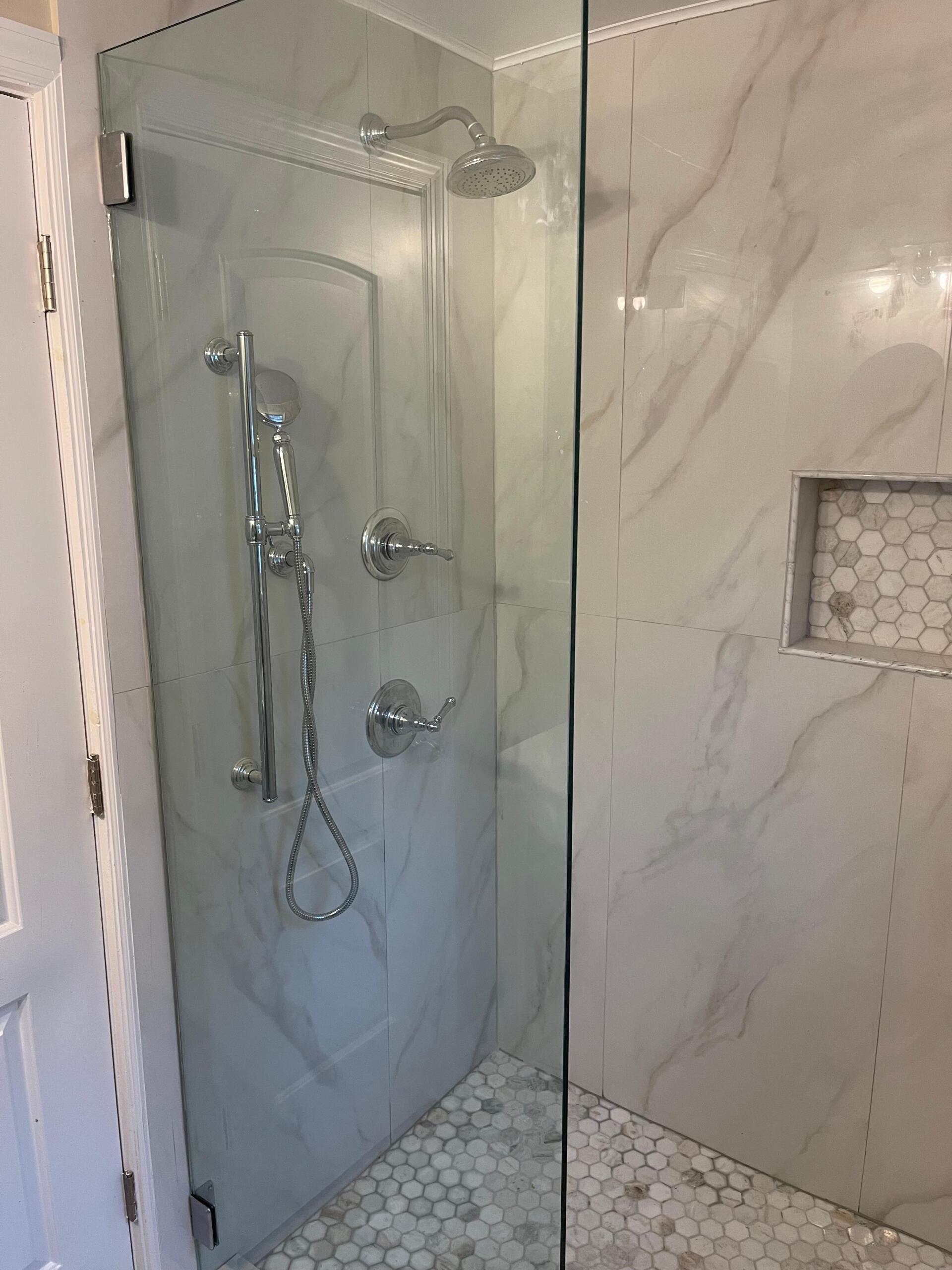 Glass shower enclosure with white marble tiles and chrome fixtures.