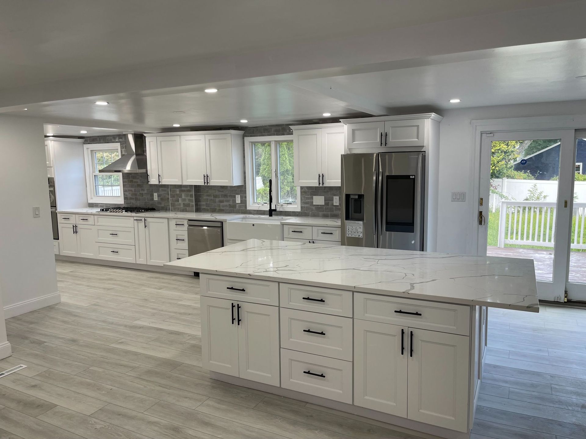 Modern white kitchen with island, stainless steel appliances, and sliding glass door to backyard.
