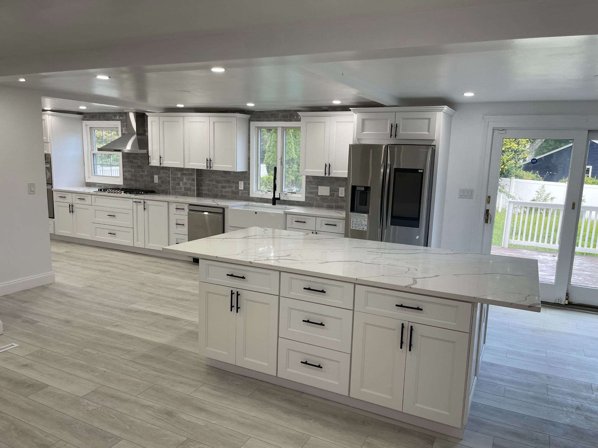 Modern white kitchen with island, stainless steel appliances, and sliding glass doors to a deck.