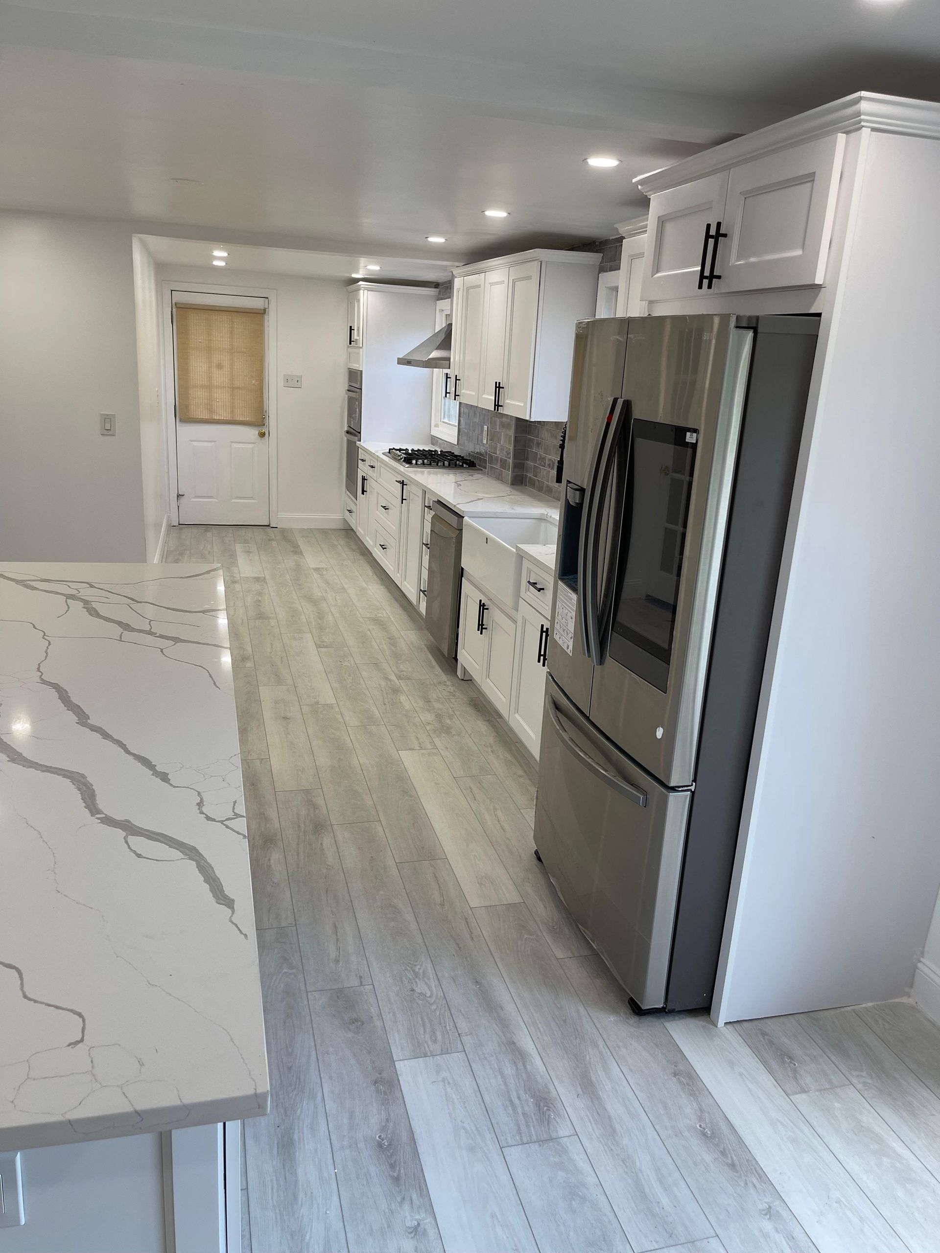 Modern white kitchen with stainless steel appliances and light wood floors.