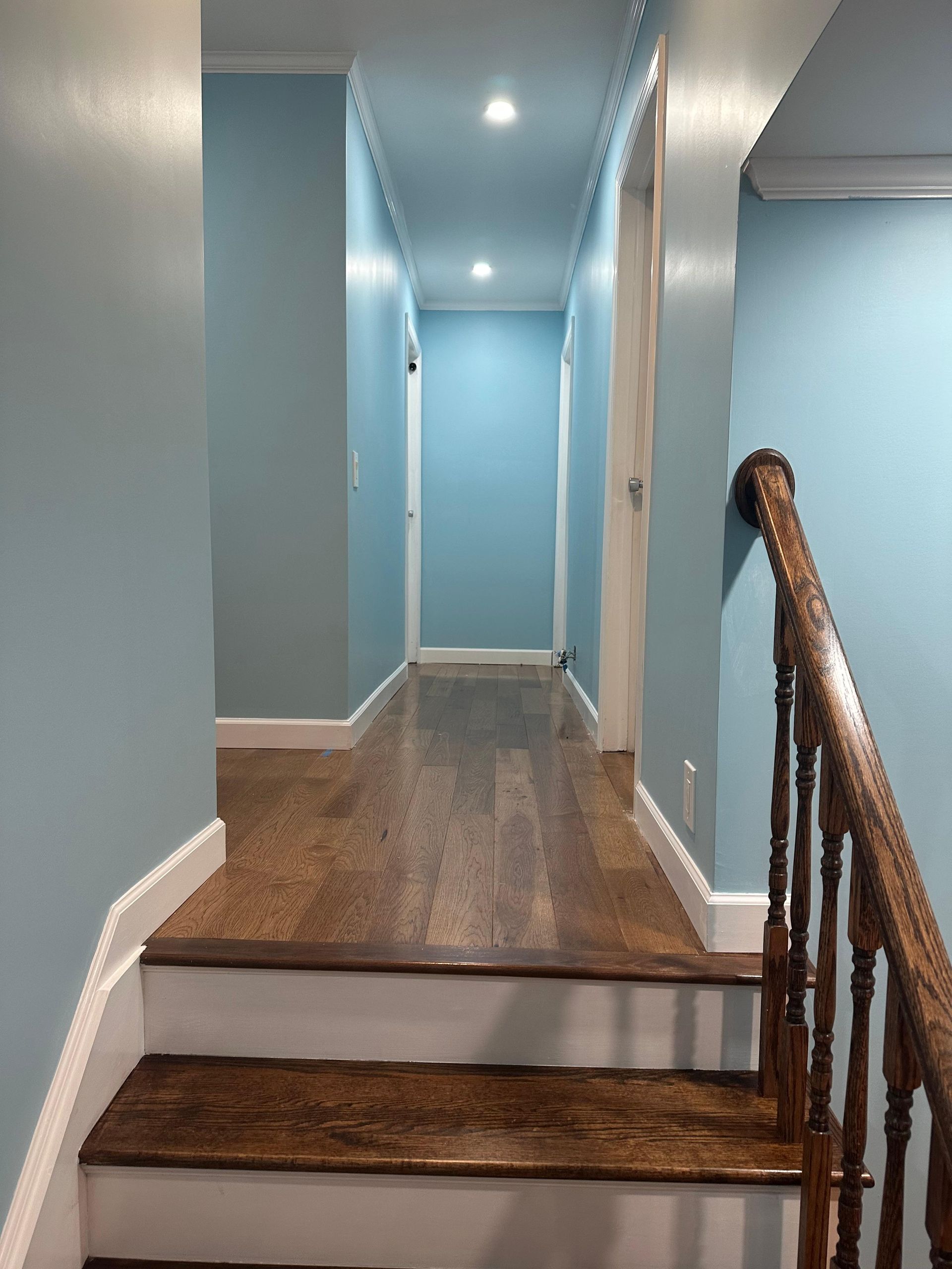 Hallway with light blue walls, wood floor, and staircase with wooden banister.