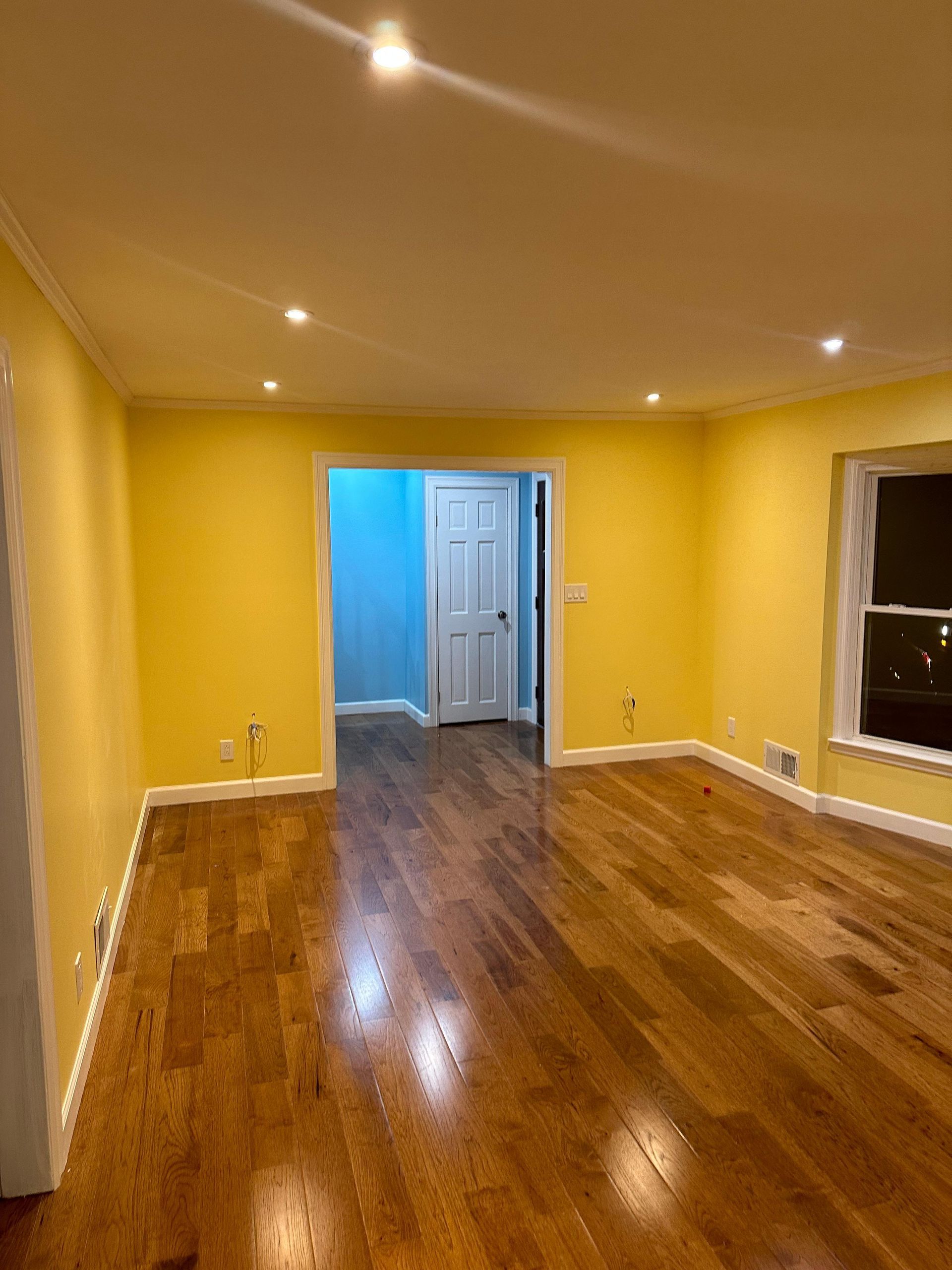 Empty room with yellow walls, hardwood floor, and a doorway leading to a blue-walled area.