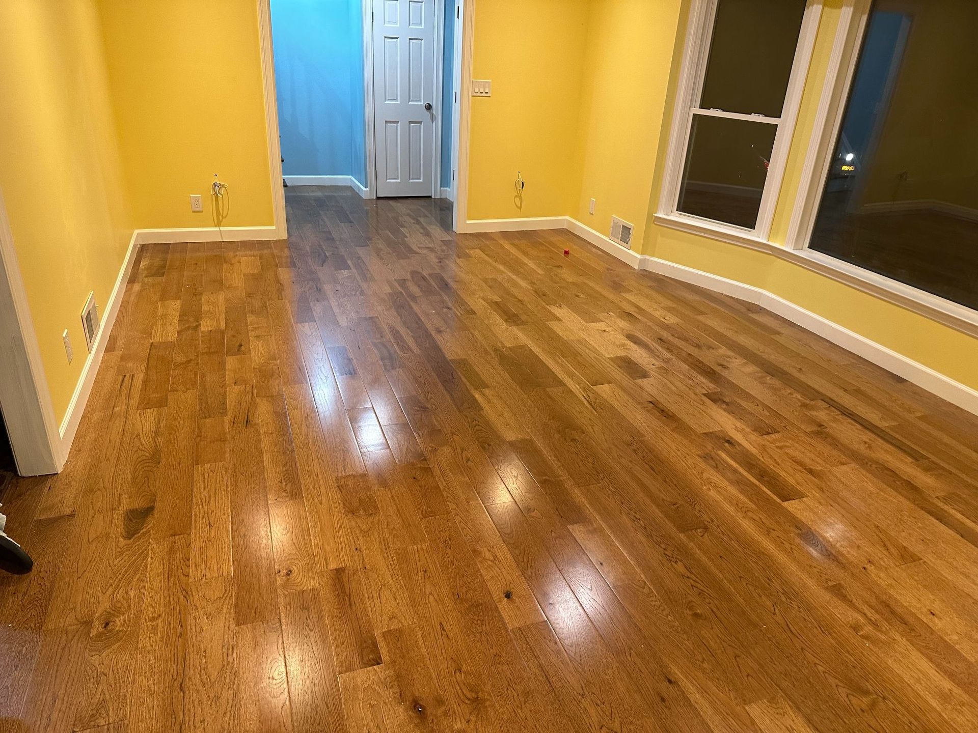 Wooden floor in room with yellow walls, white trim, and a window.