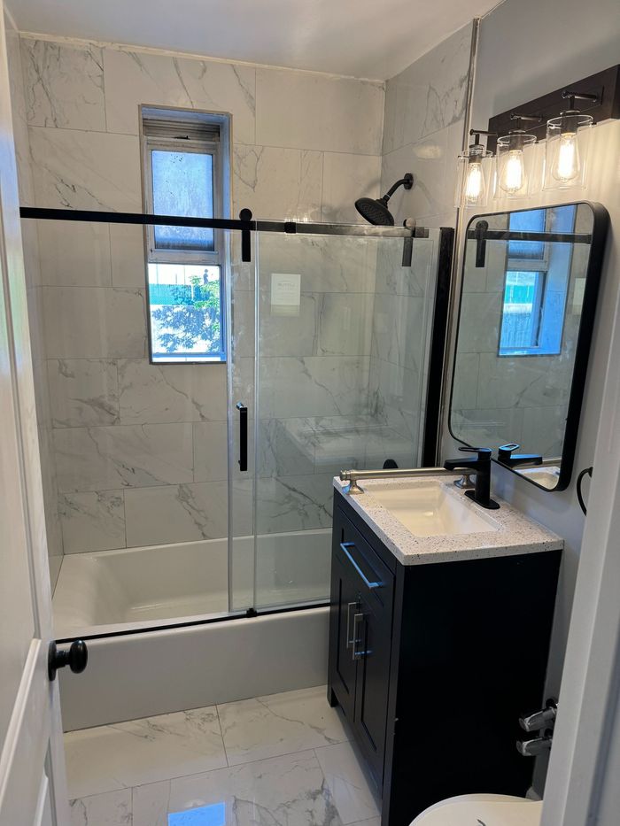 Modern bathroom with marble tile, black vanity, shower with sliding glass door, and black fixtures.