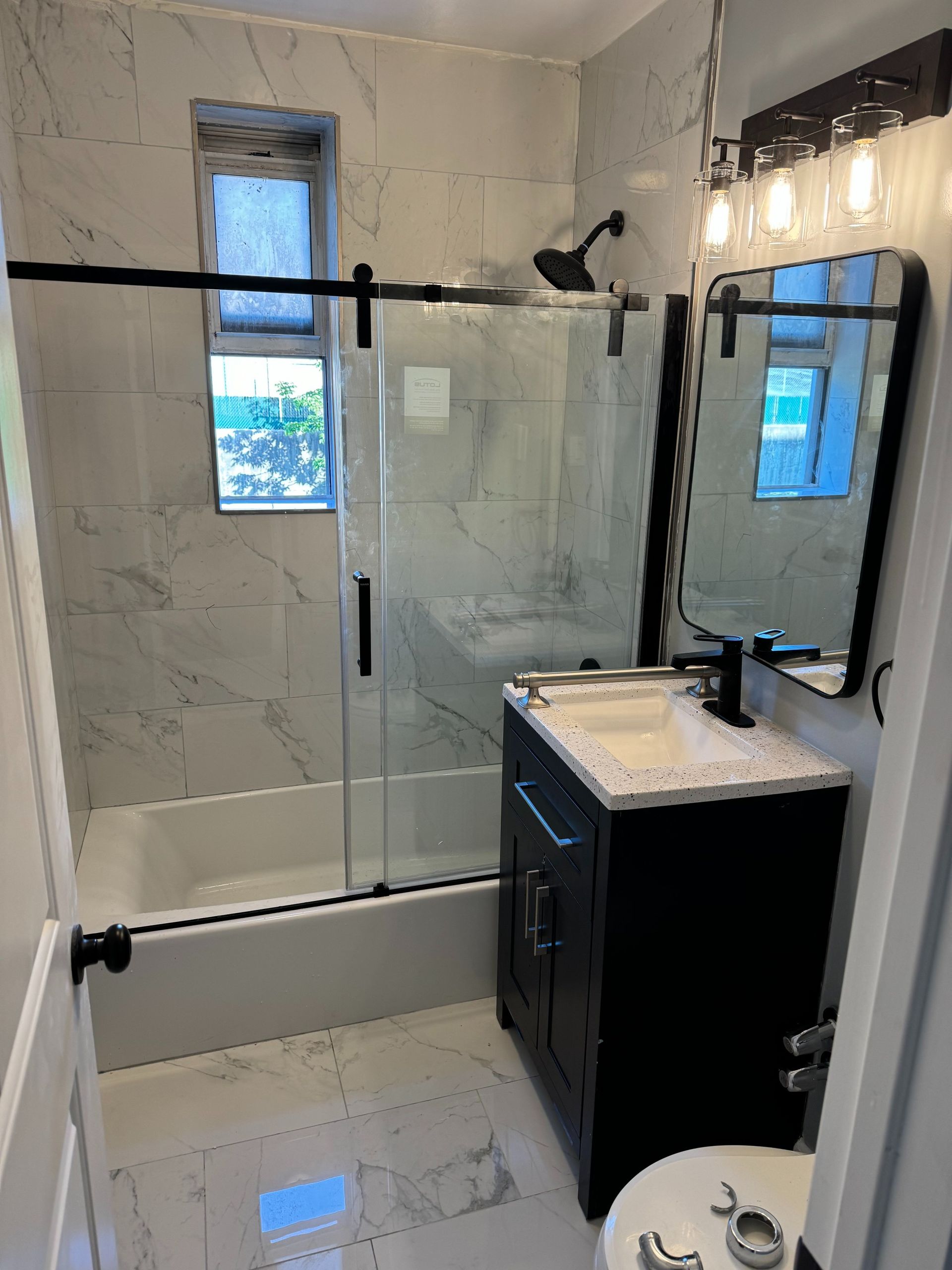 Modern bathroom with marble tile, black fixtures, shower, vanity, and toilet.
