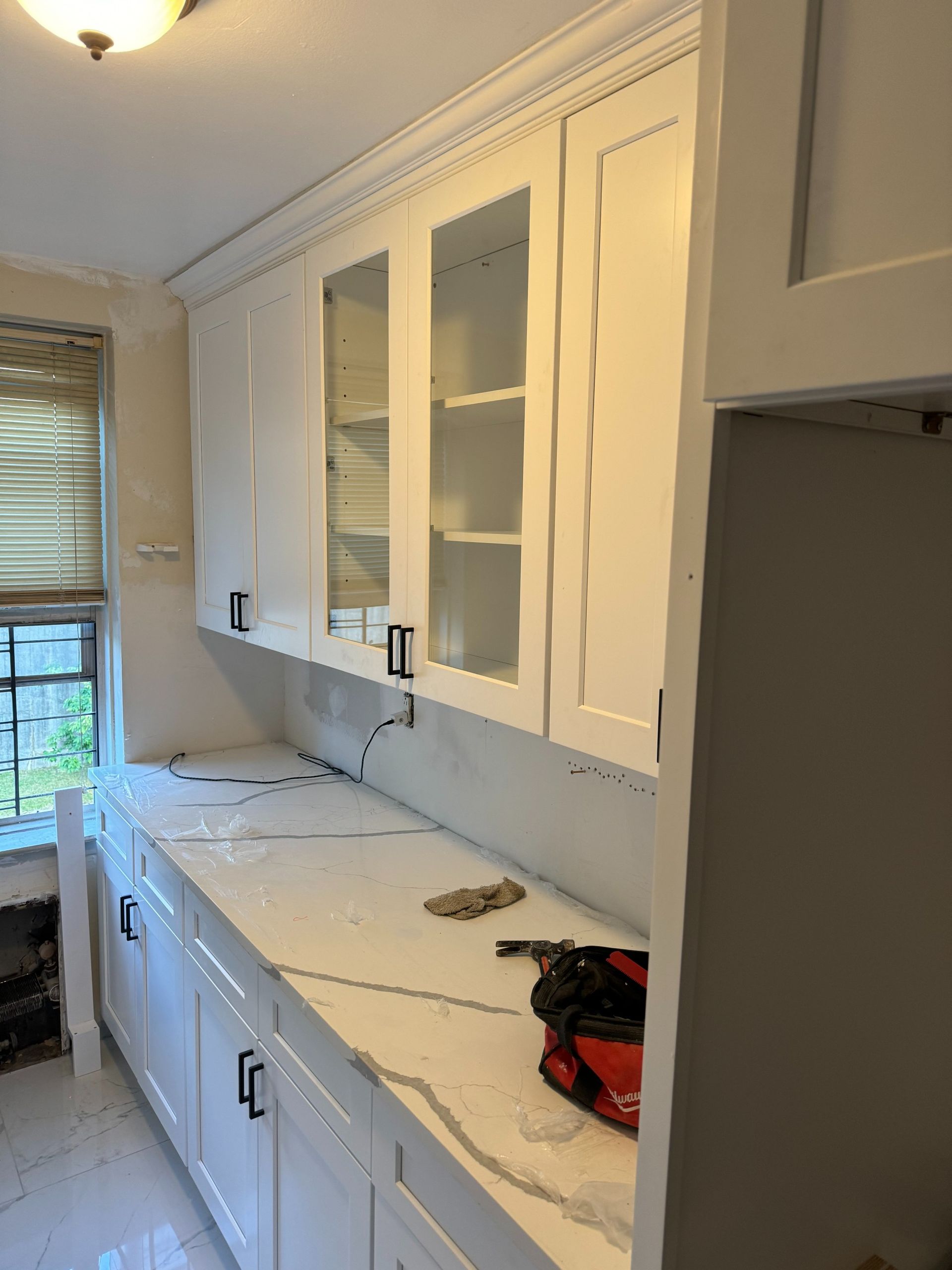 White kitchen cabinets with black handles, a white countertop, and a window.