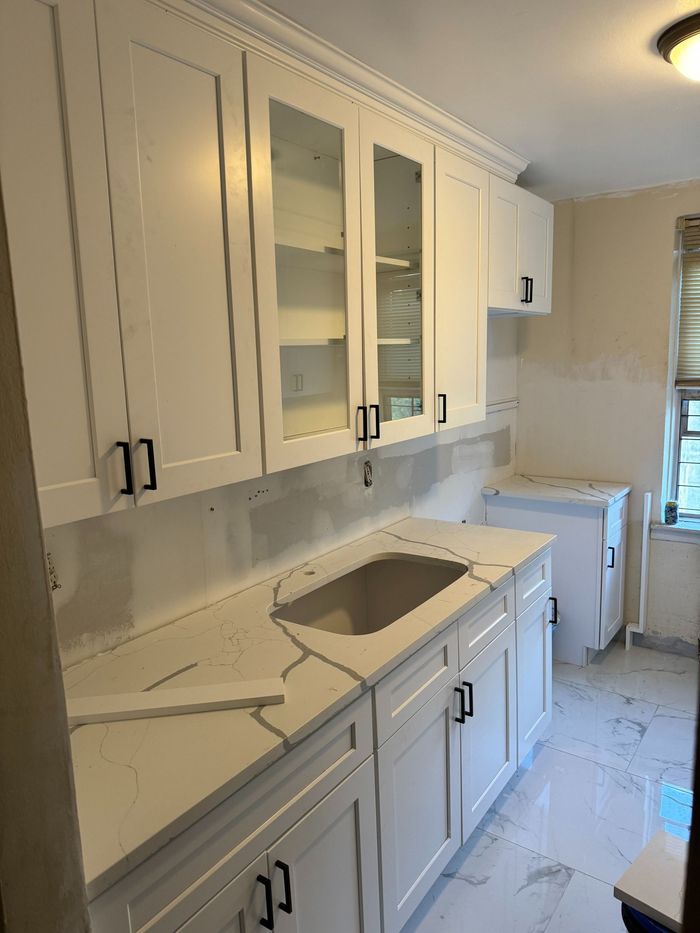 White kitchen cabinets with black handles, a white countertop, and a sink.