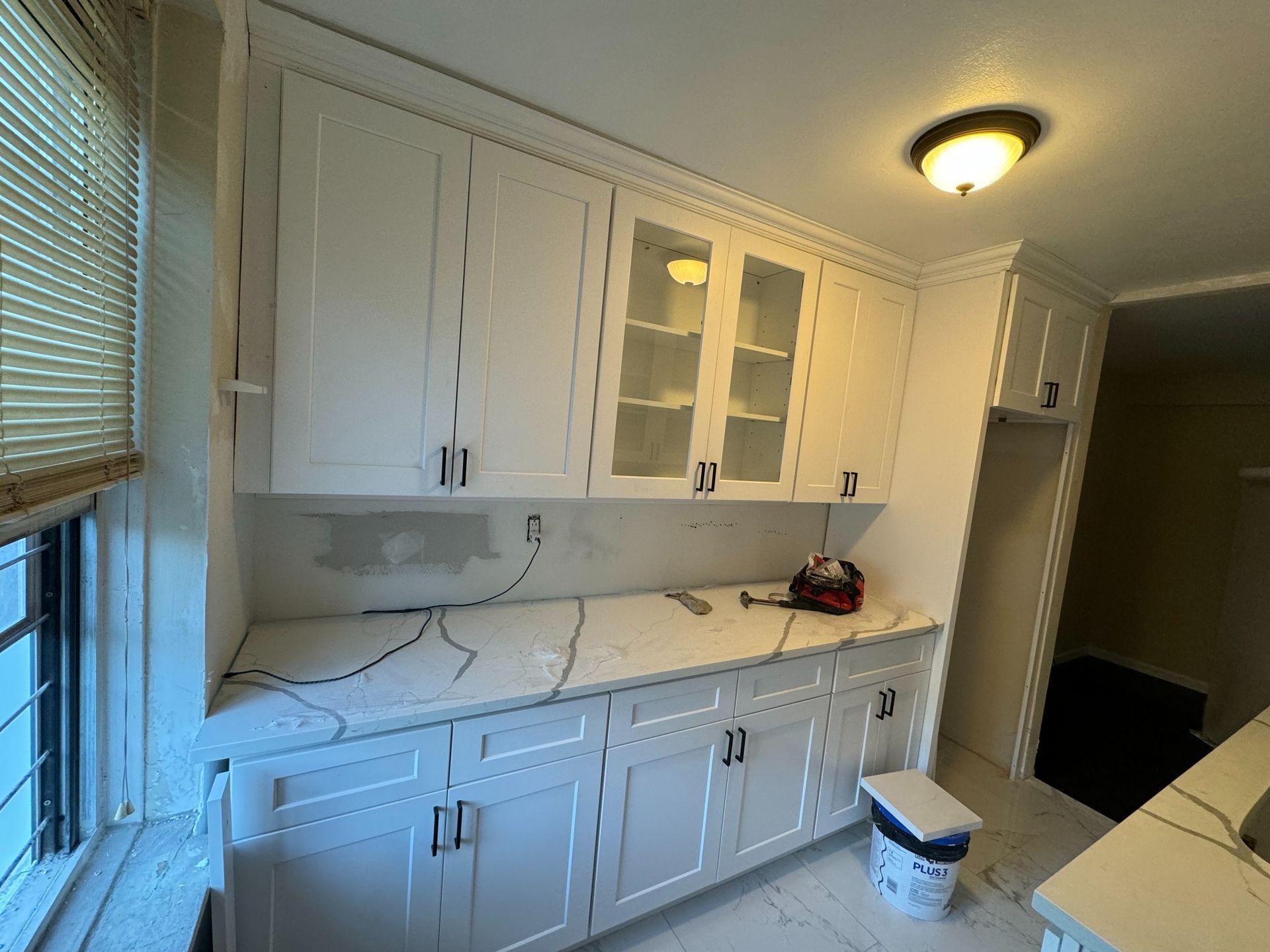 White kitchen cabinets with black hardware and a marble countertop. A window on the left.
