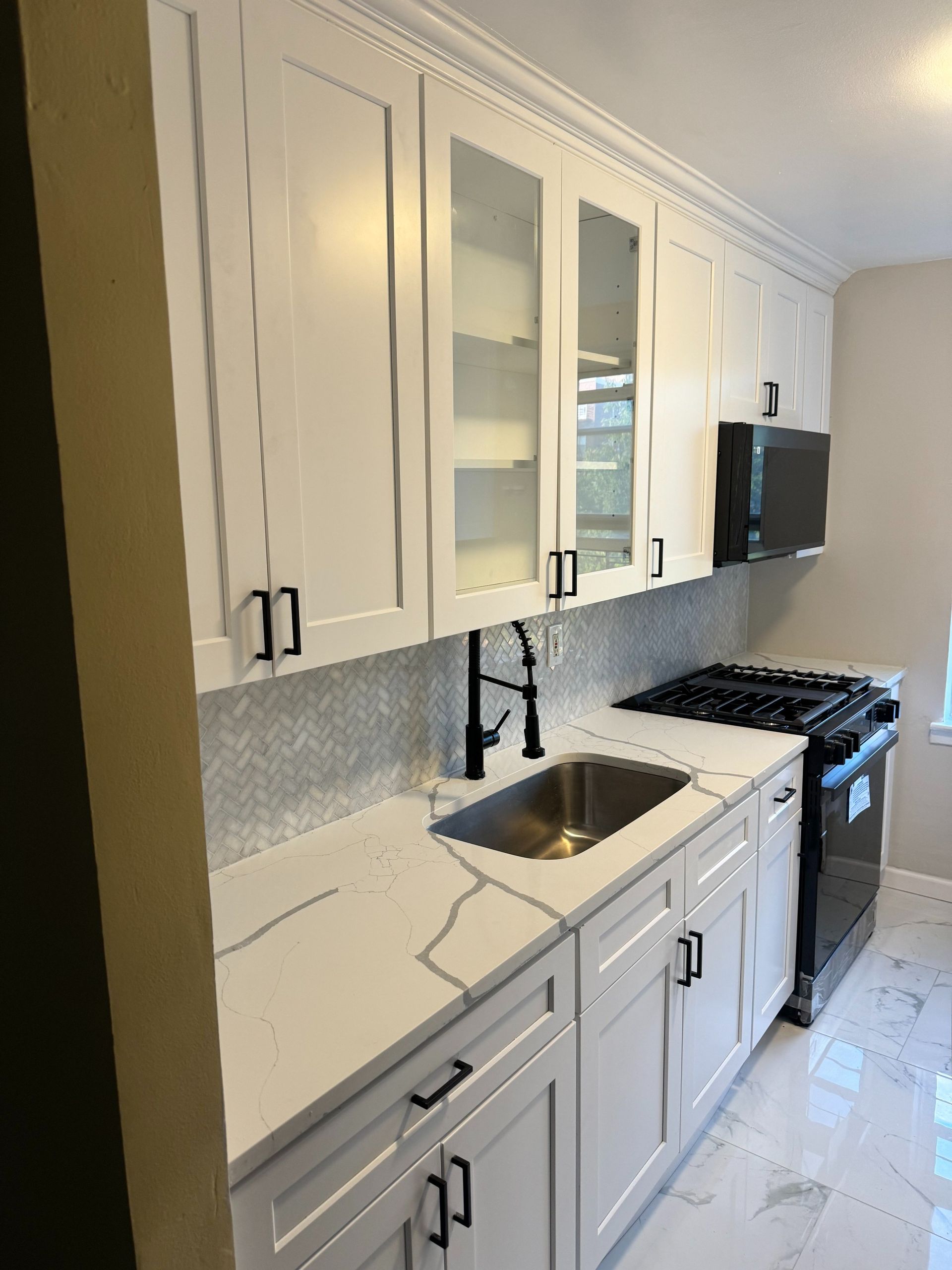 White kitchen with cabinets, countertops, sink, and stovetop. Black hardware and appliances.