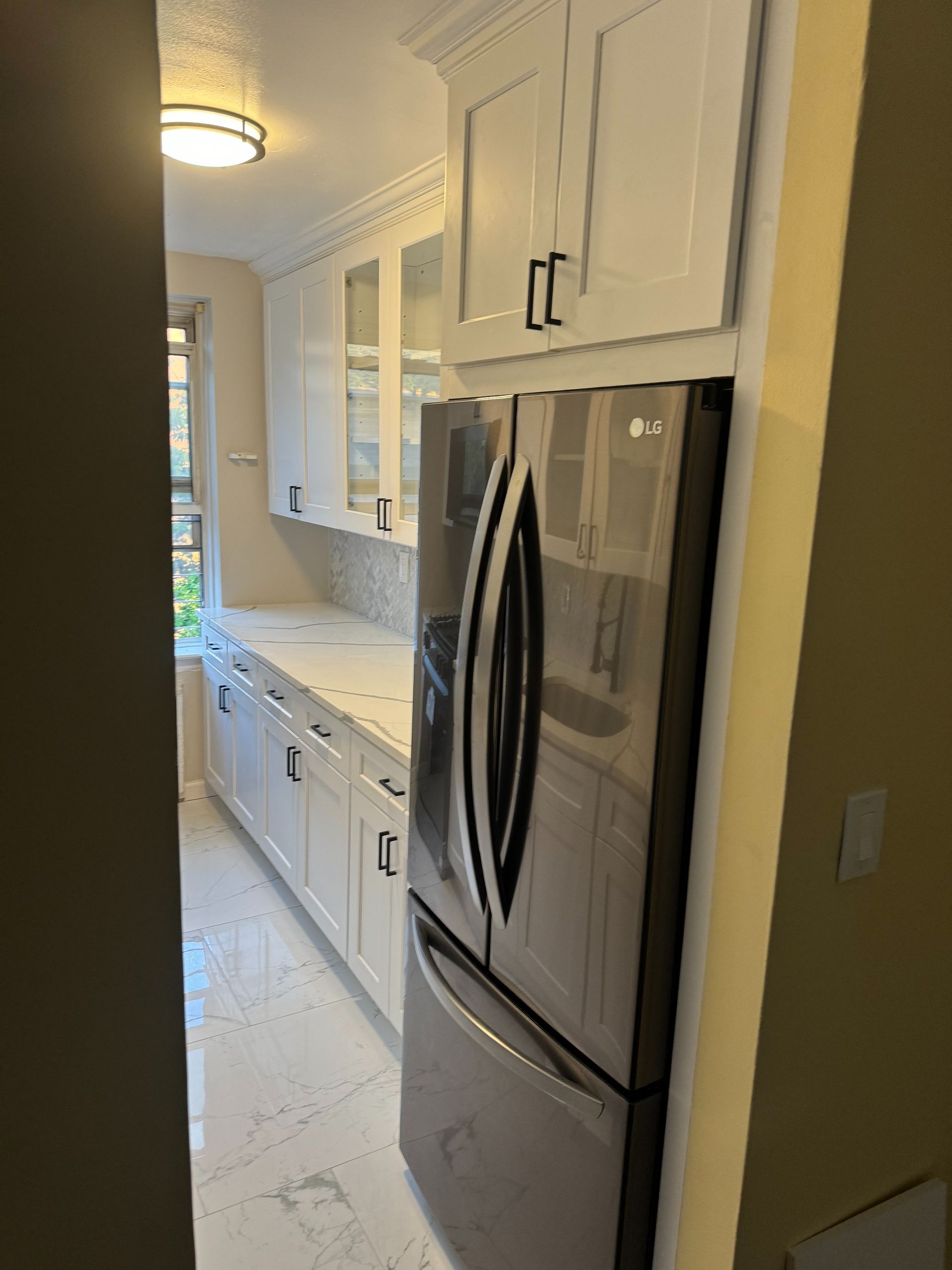 White kitchen with stainless steel refrigerator, marble countertops, and cabinets.
