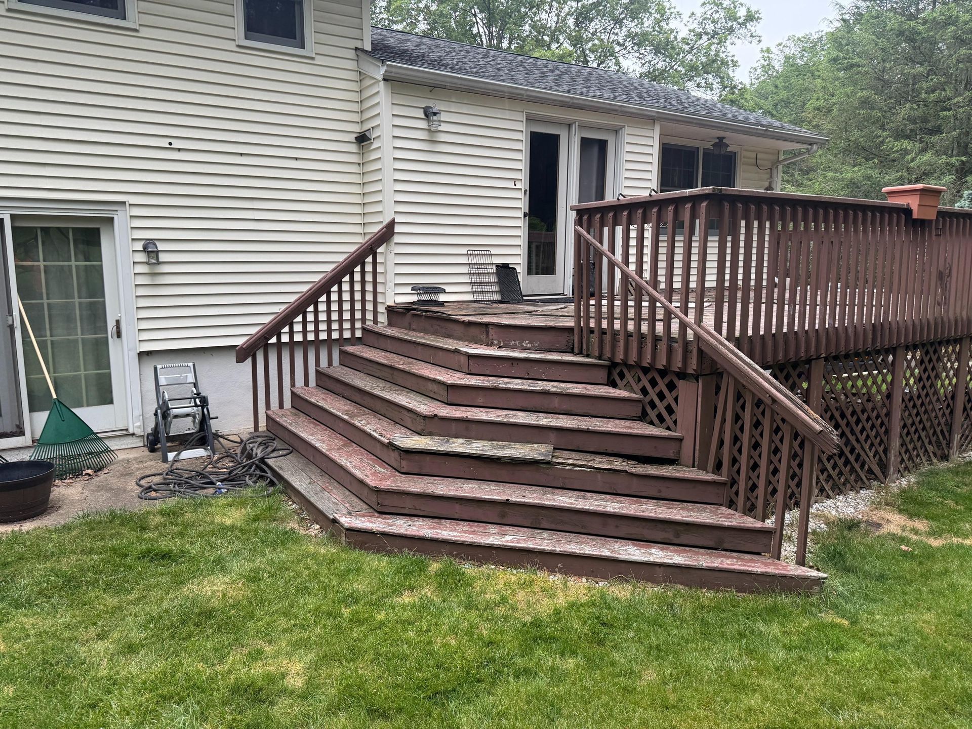 Brown wooden deck with steps leading down to a grassy yard. The house has white siding.