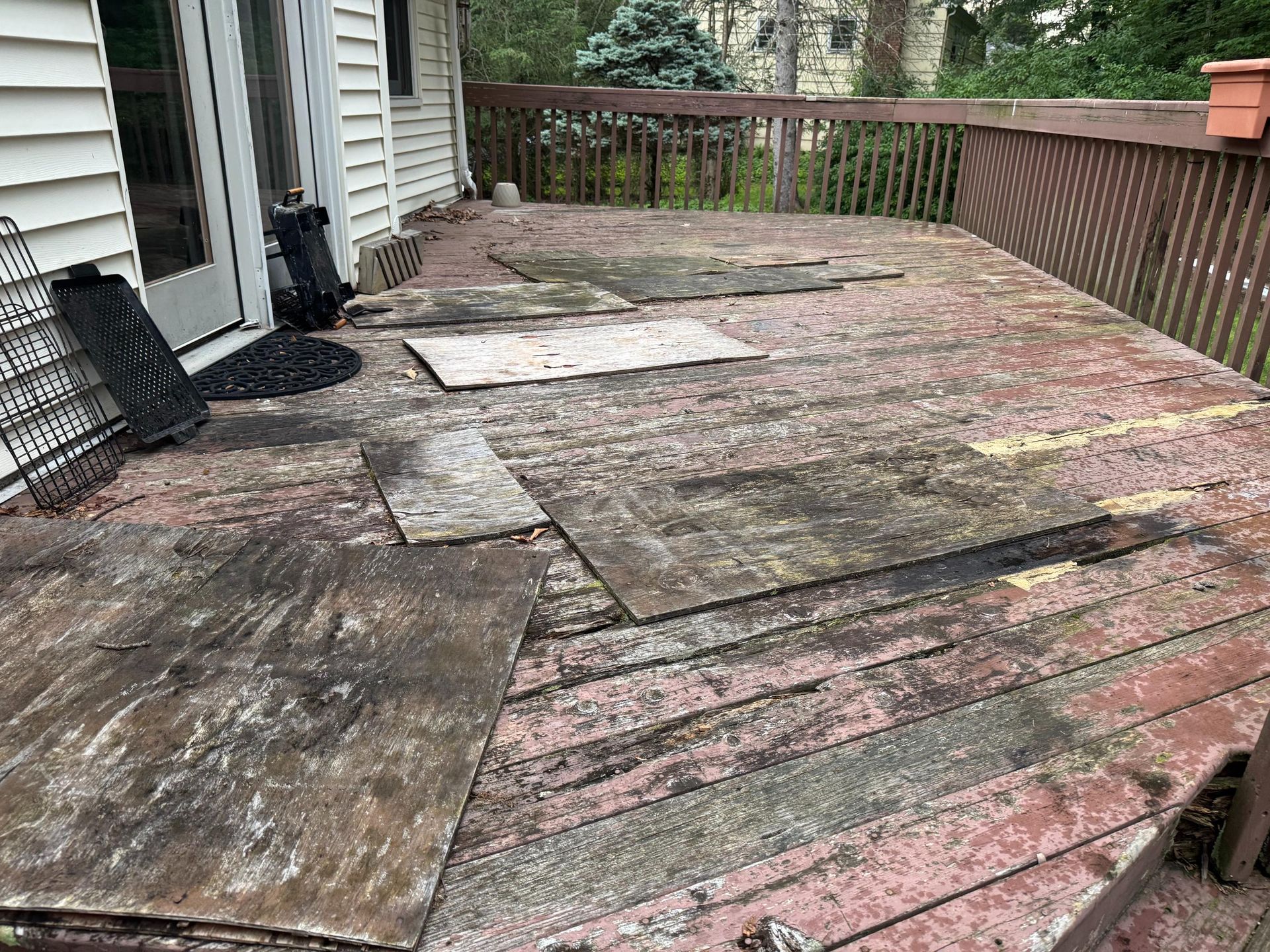Weathered wooden deck with damaged boards, next to a white house.