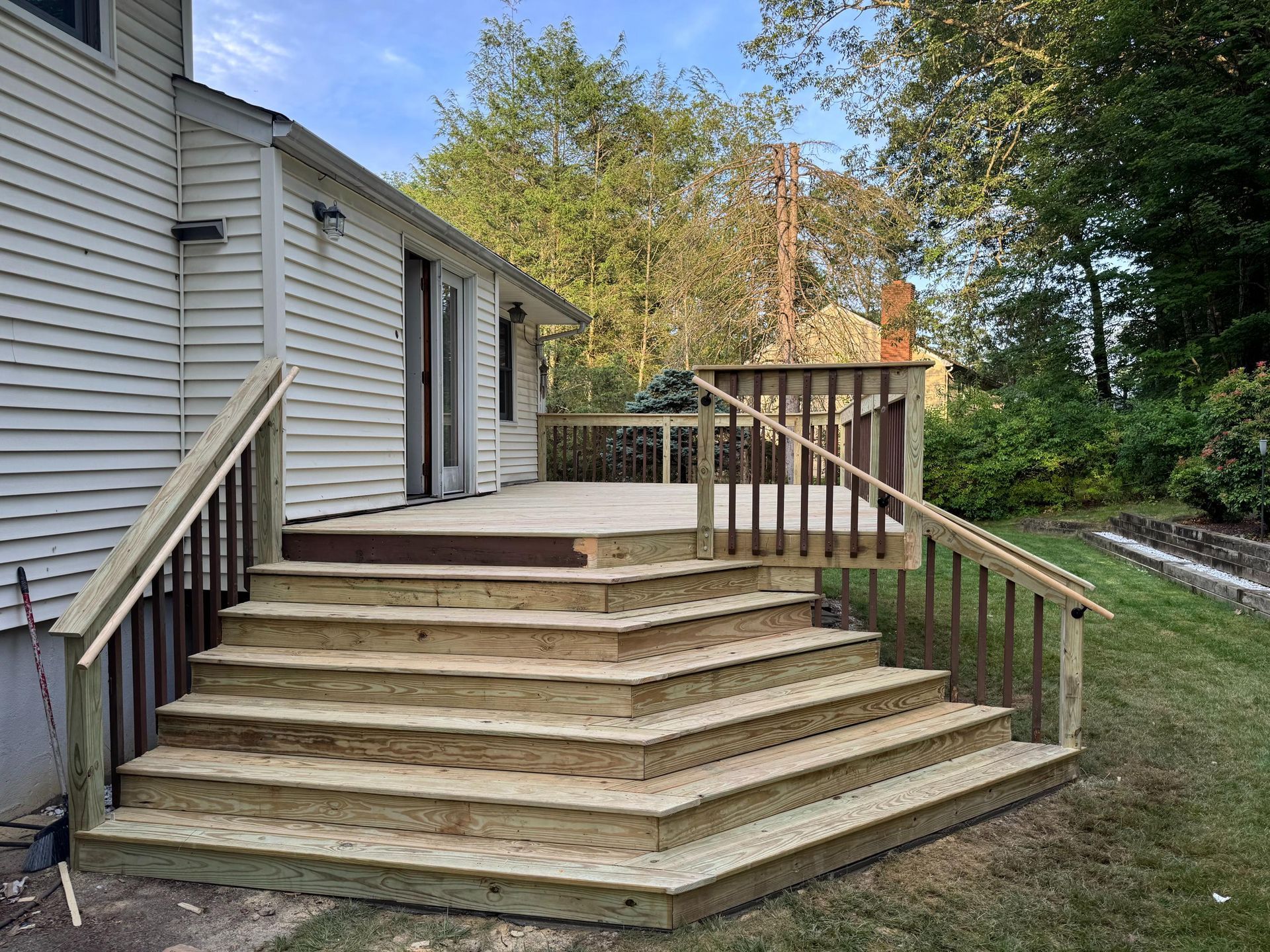 Wooden deck with multiple steps and railings attached to a house with white siding.