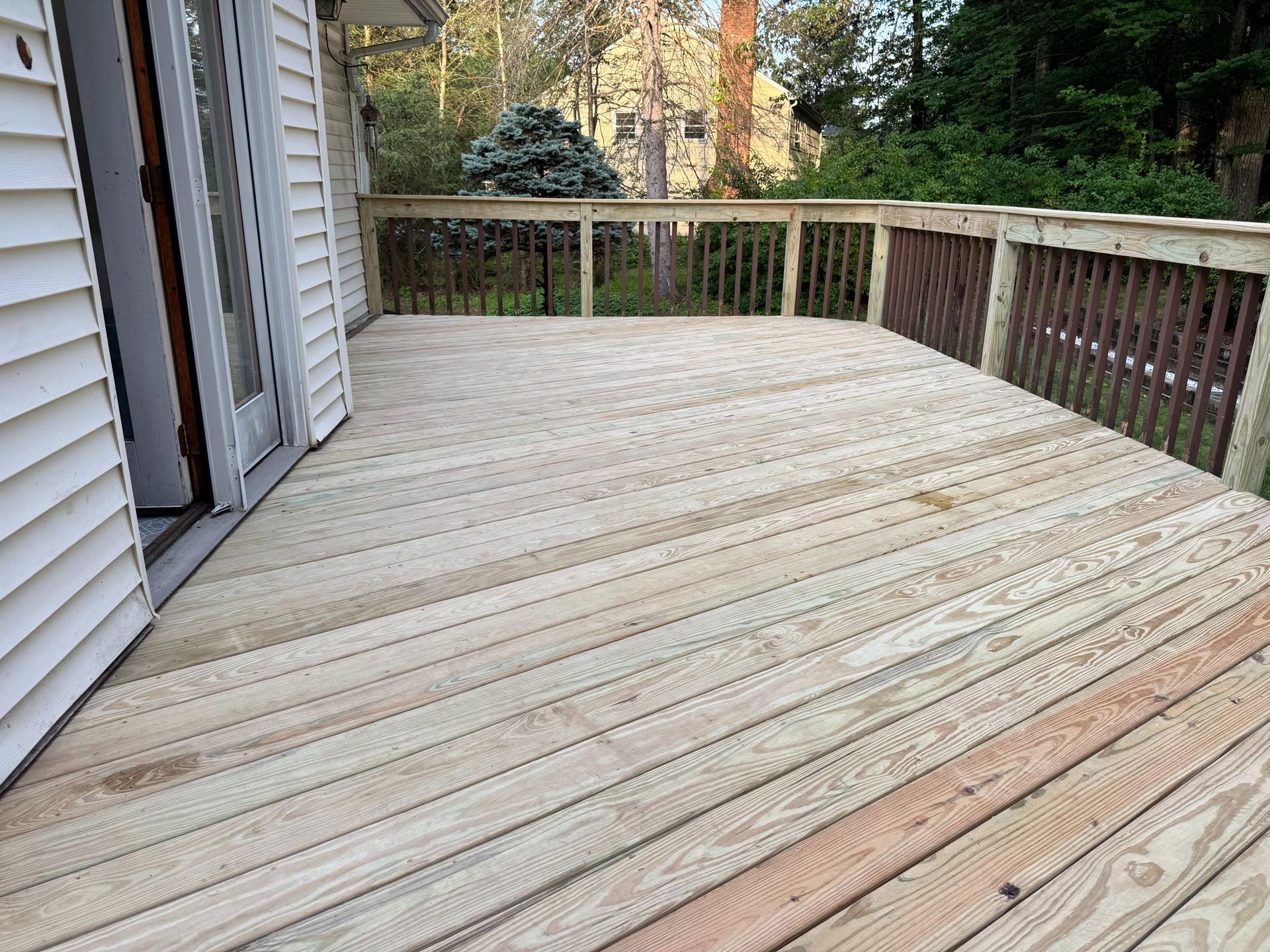 Wooden deck with railing attached to a house. Sunlight illuminates the boards.