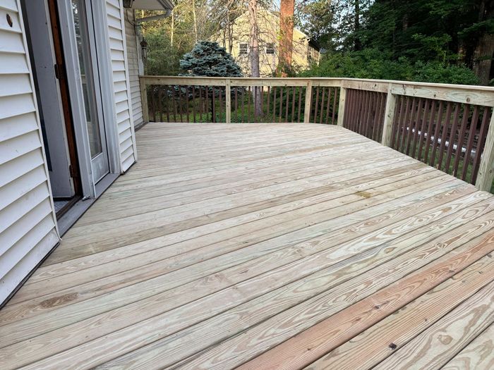 Wooden deck with railing attached to a house. Sunlight illuminates the boards.