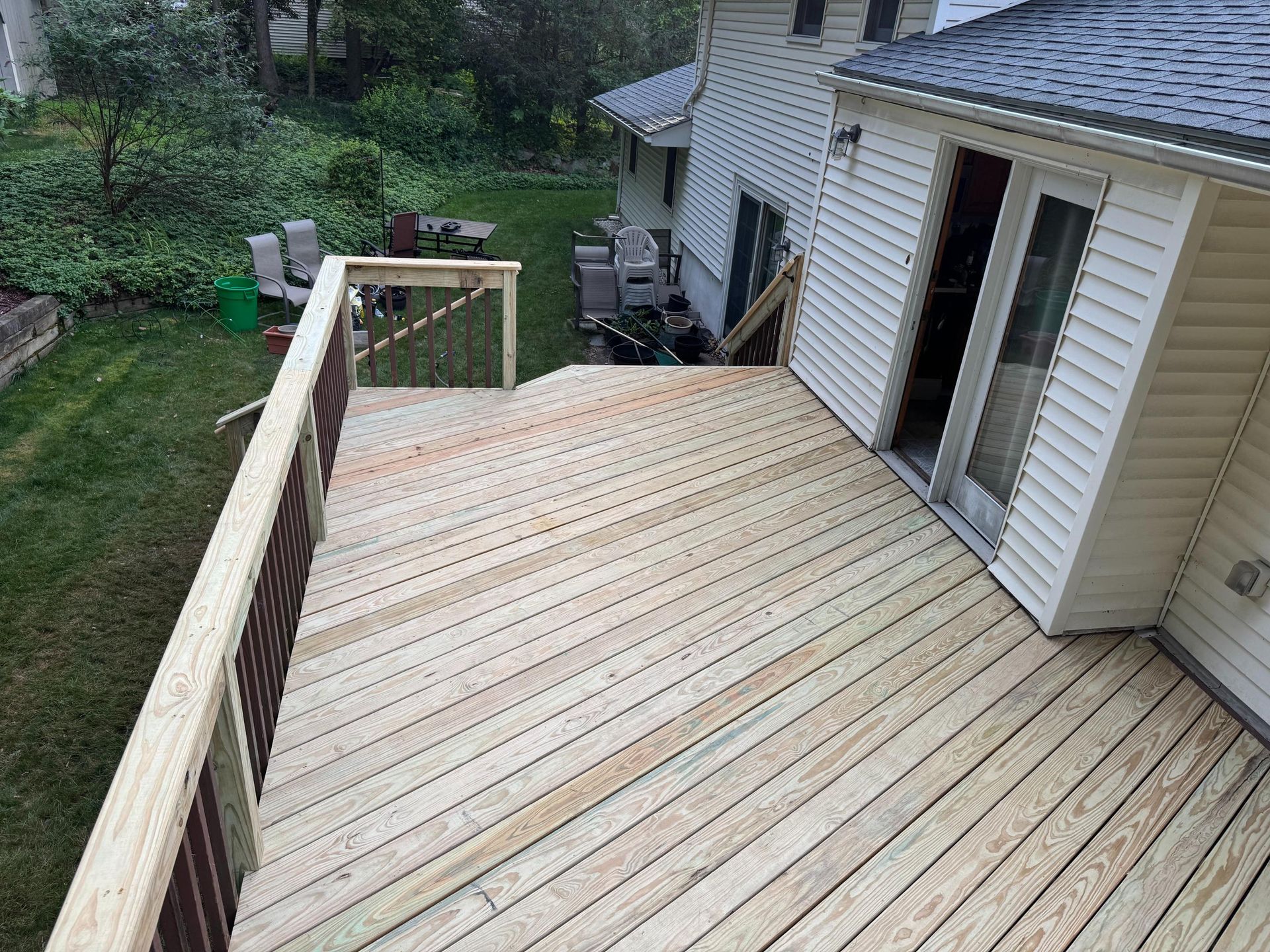 Wooden deck attached to a white house with glass doors, overlooking a backyard with grass and trees.